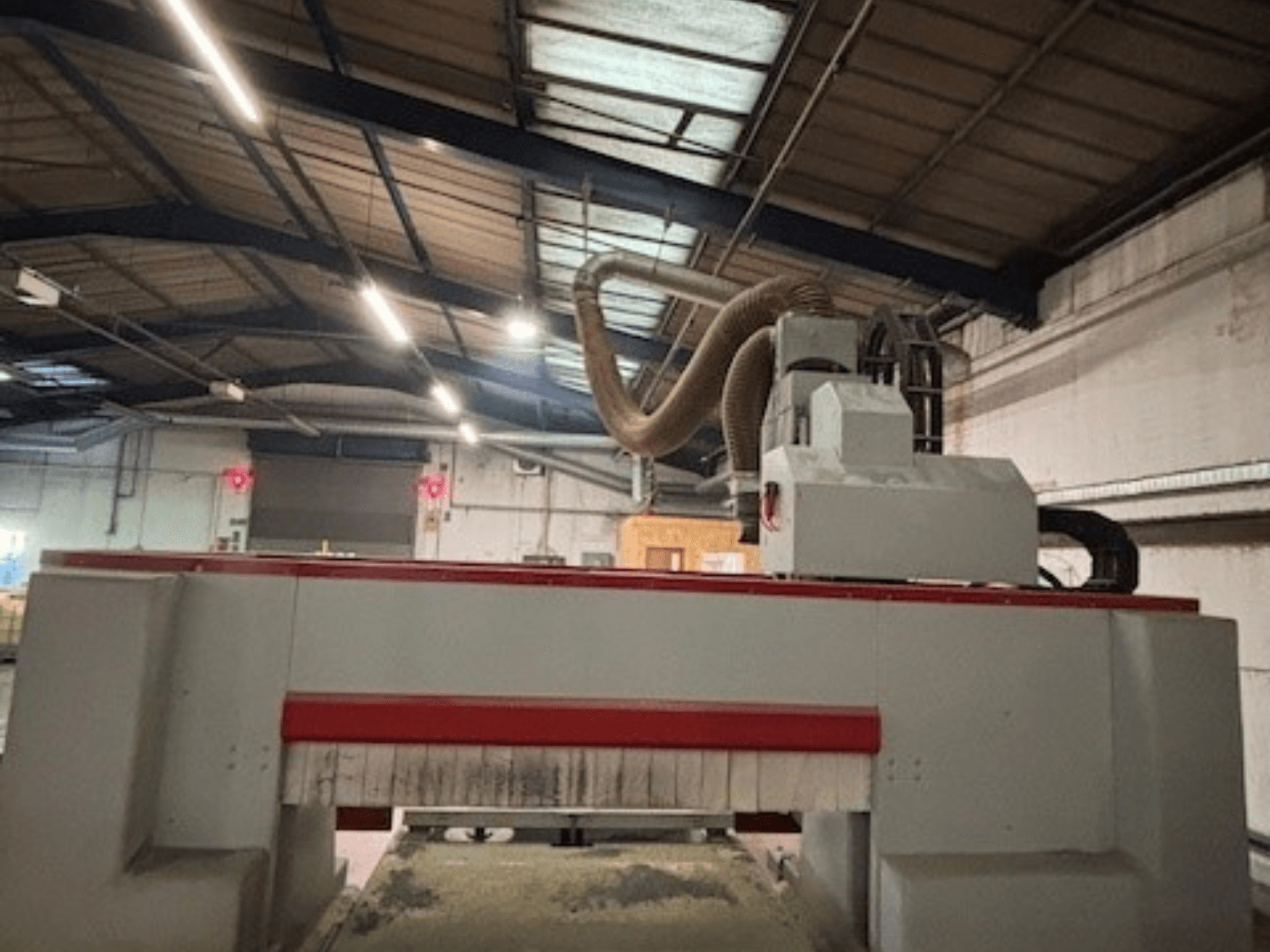 Frezarka CNC w warsztacie, widok z boku podkreślający czerwono-szarą konstrukcję, dołączony system odsysania pyłu.