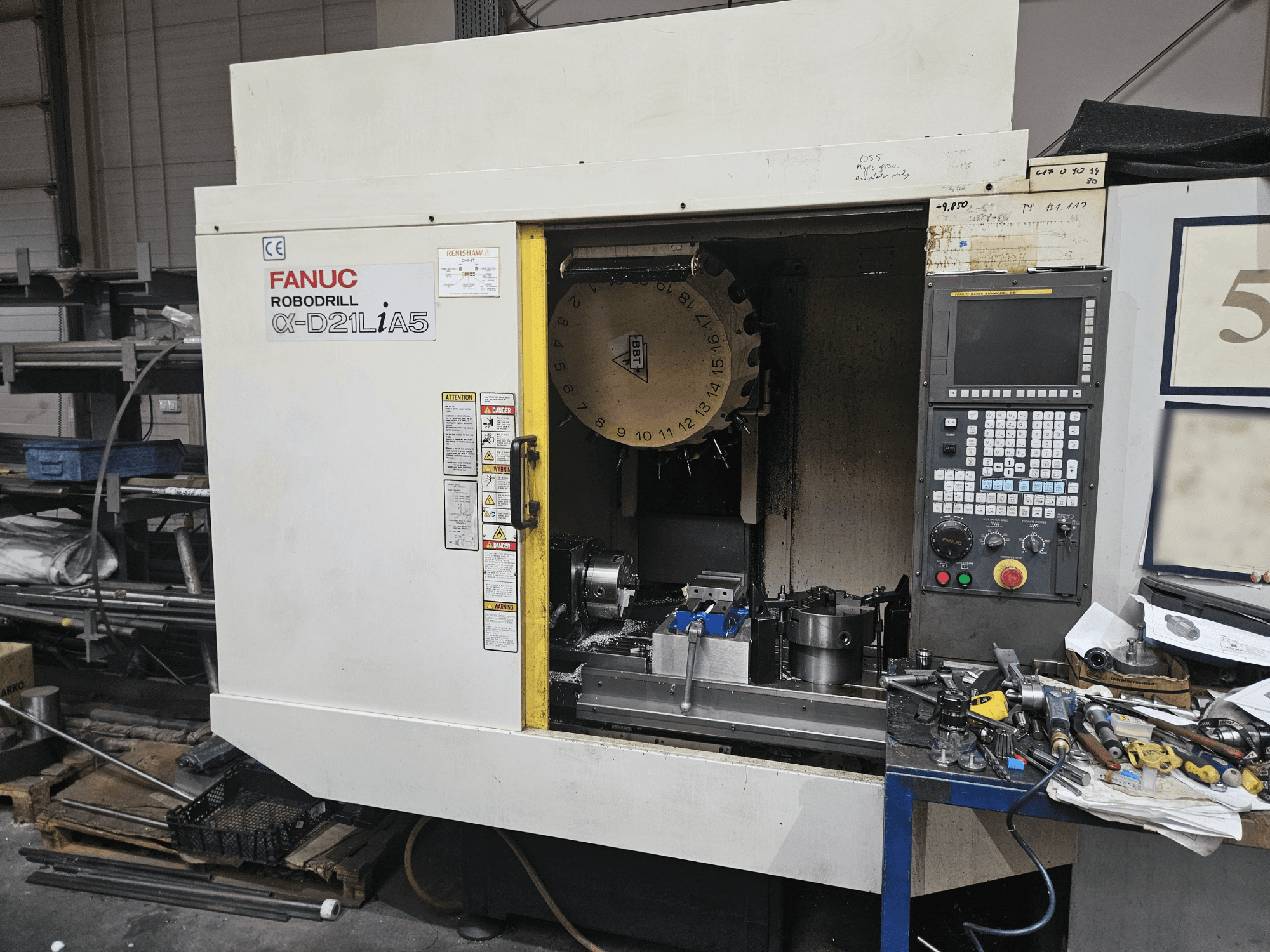 FANUC Robodrill α-D21LiA5, widok z przodu przedstawiający uchwyt narzędziowy i panel sterowania, otoczony narzędziami i sprzętem w warsztacie.