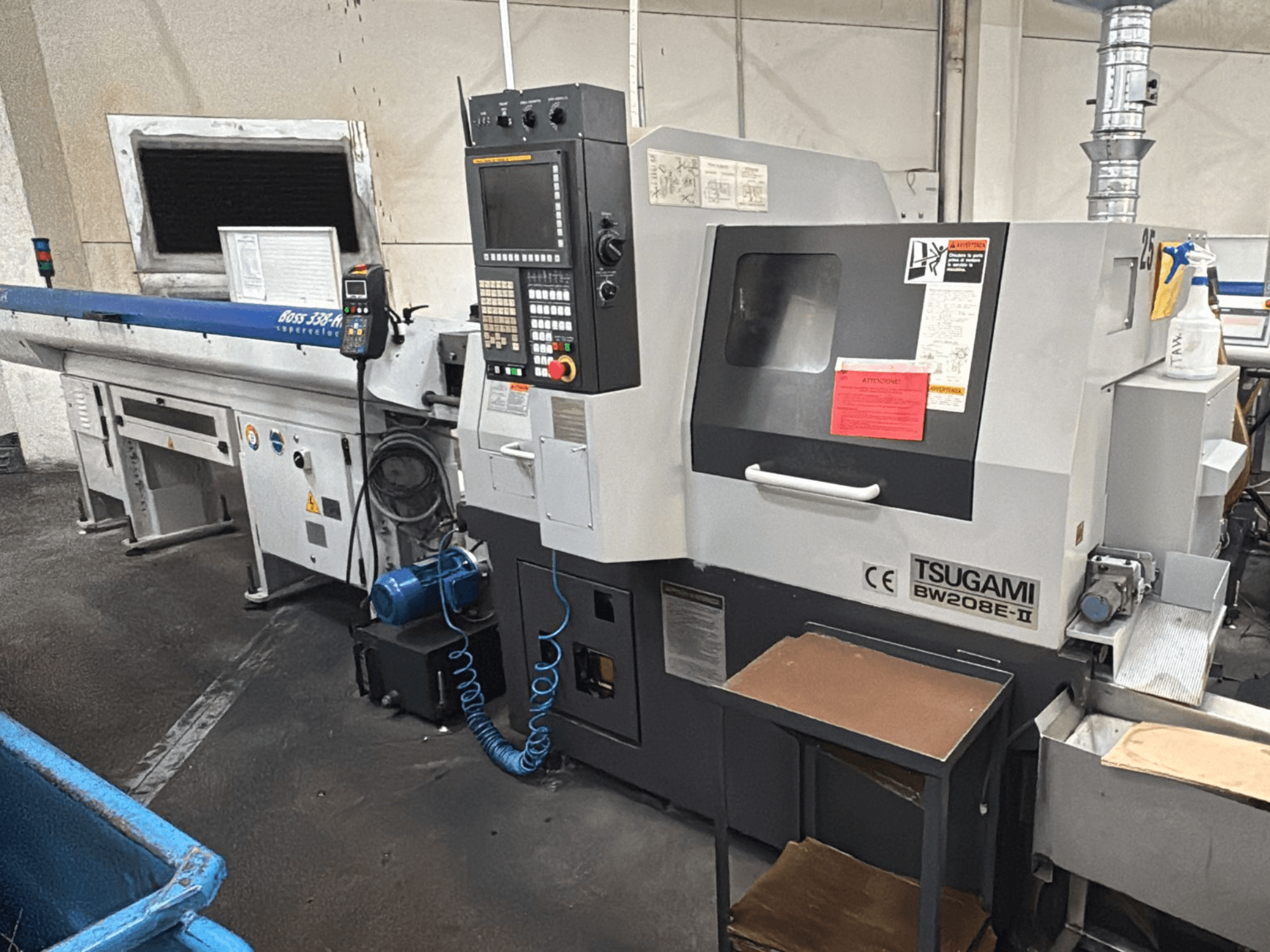 Maszyna CNC Tsugami BW208E-II w warsztacie, pokazana z przodu, z widocznym panelem sterowania i etykietami bezpieczeństwa.