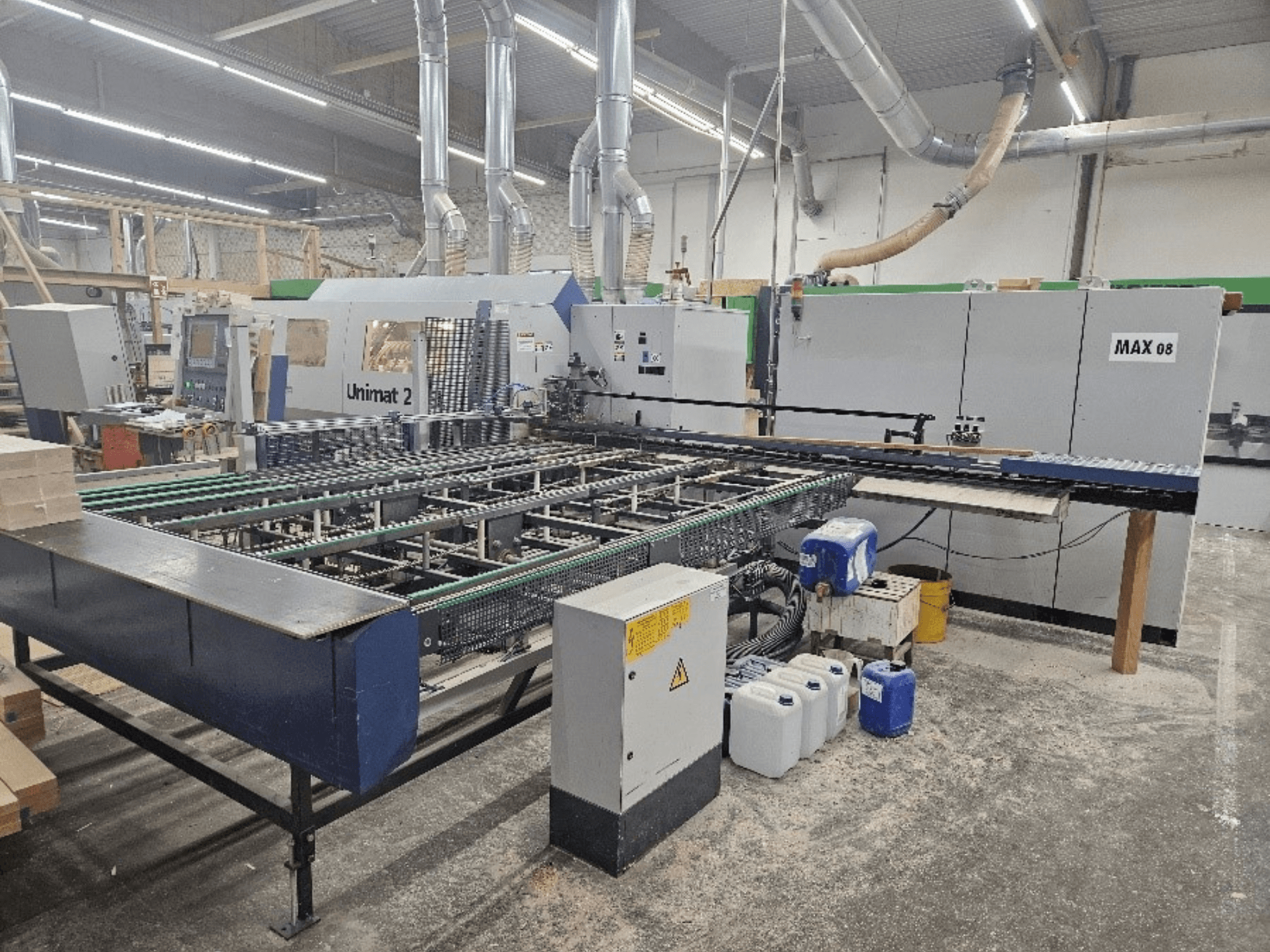 Widok z boku maszyny CNC Unimat 2 w warsztacie, z przenośnikami taśmowymi i komponentami technicznymi z widoczną jednostką Max 08.