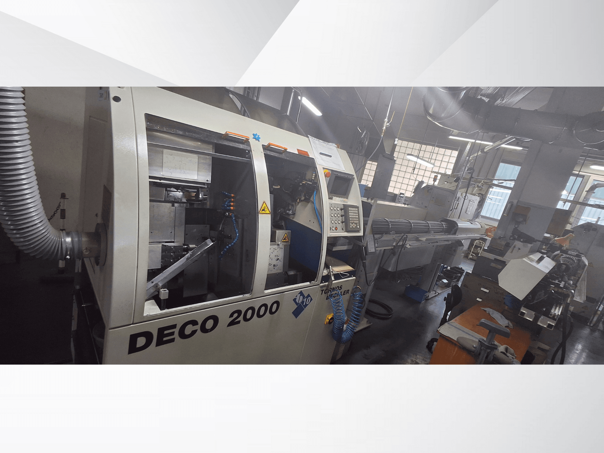 Maszyna CNC DECO 2000 w warsztacie, widok z przodu, elementy sterujące i konfiguracja długiego przedmiotu obrabianego po prawej stronie.