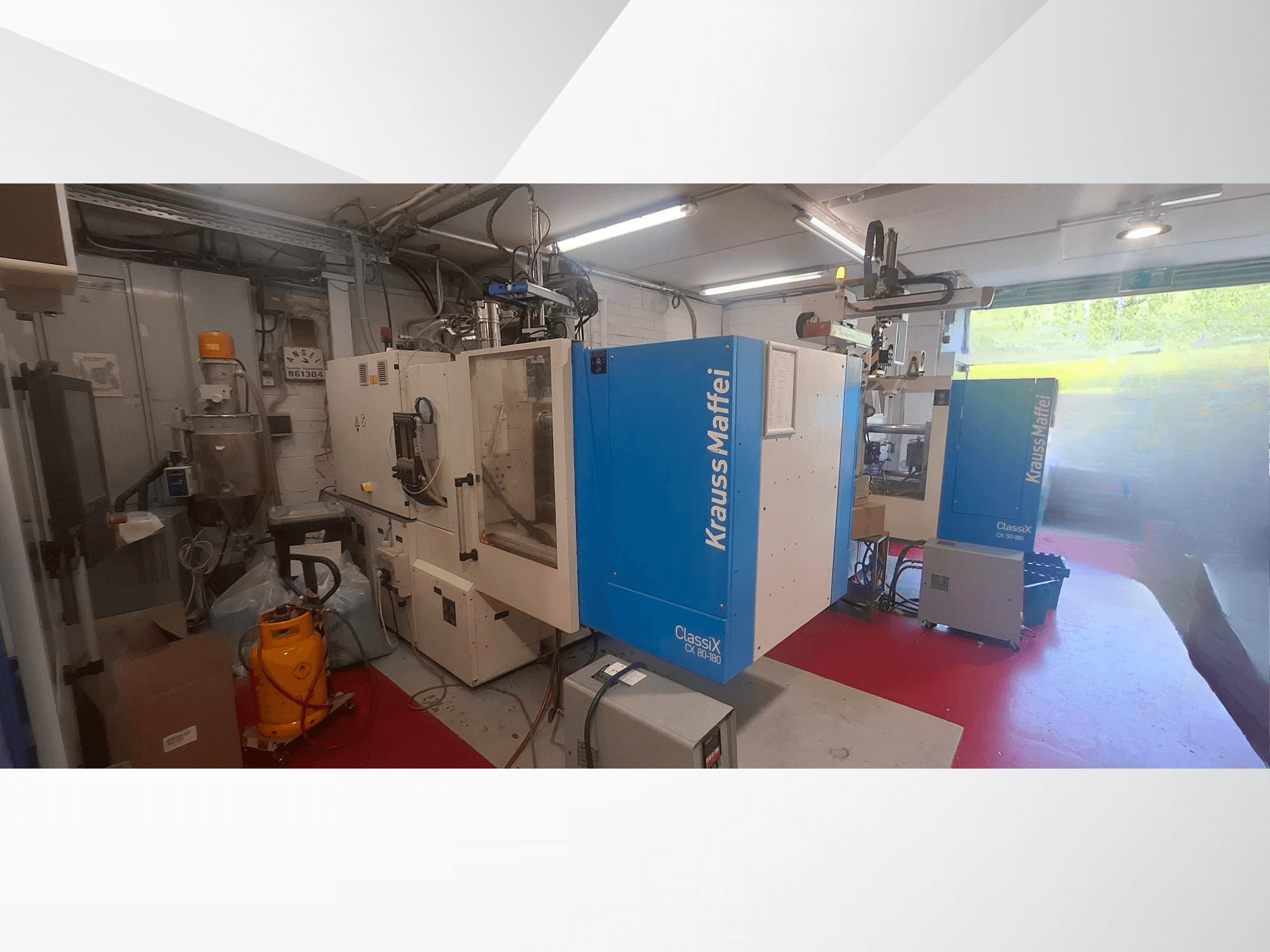 Hydrauliczna wtryskarka Krauss Maffei CX 80-180, widok z przodu, w otoczeniu przemysłowym wraz z otaczającym ją wyposażeniem.