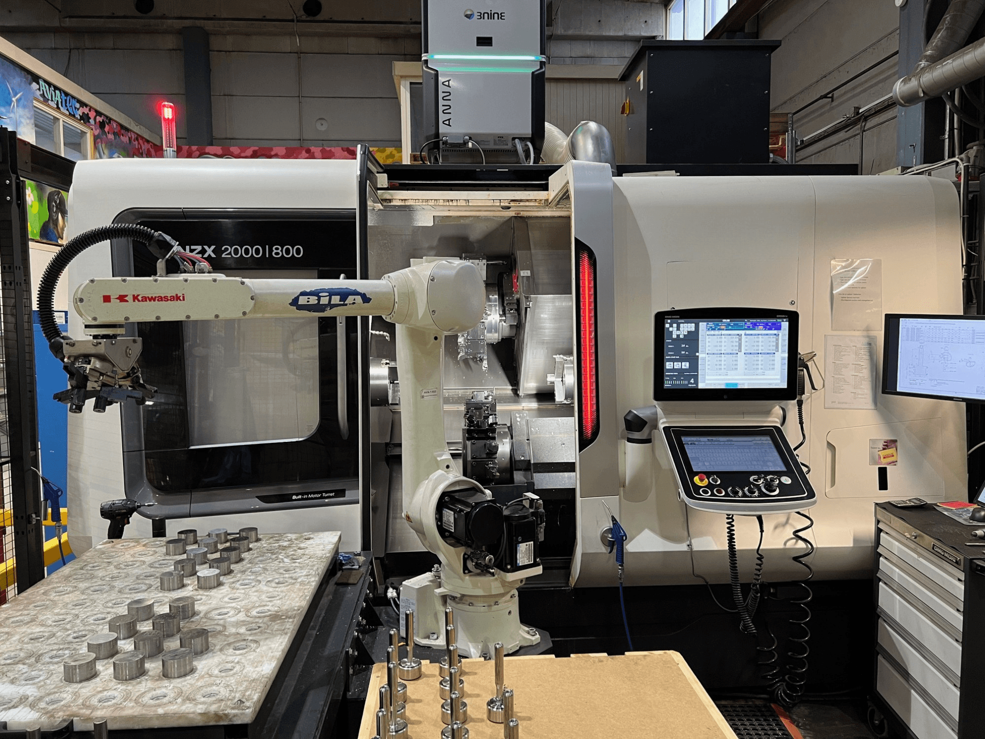 Pozioma tokarka DMG MORI NZX 2000/800SY w warsztacie, z widocznym ramieniem robota firmy Kawasaki i panelem sterowania.