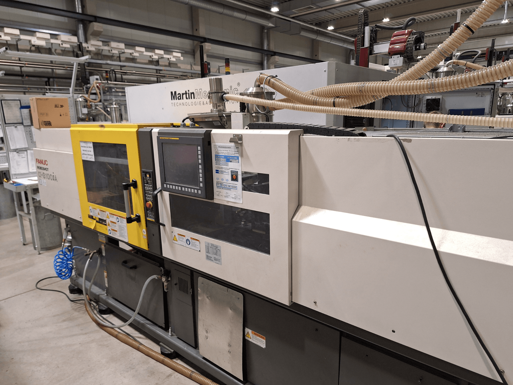 Elektryczna wtryskarka FANUC Roboshot S100iA, widok z boku, wyposażona w ekran dotykowy i etykiety bezpieczeństwa.