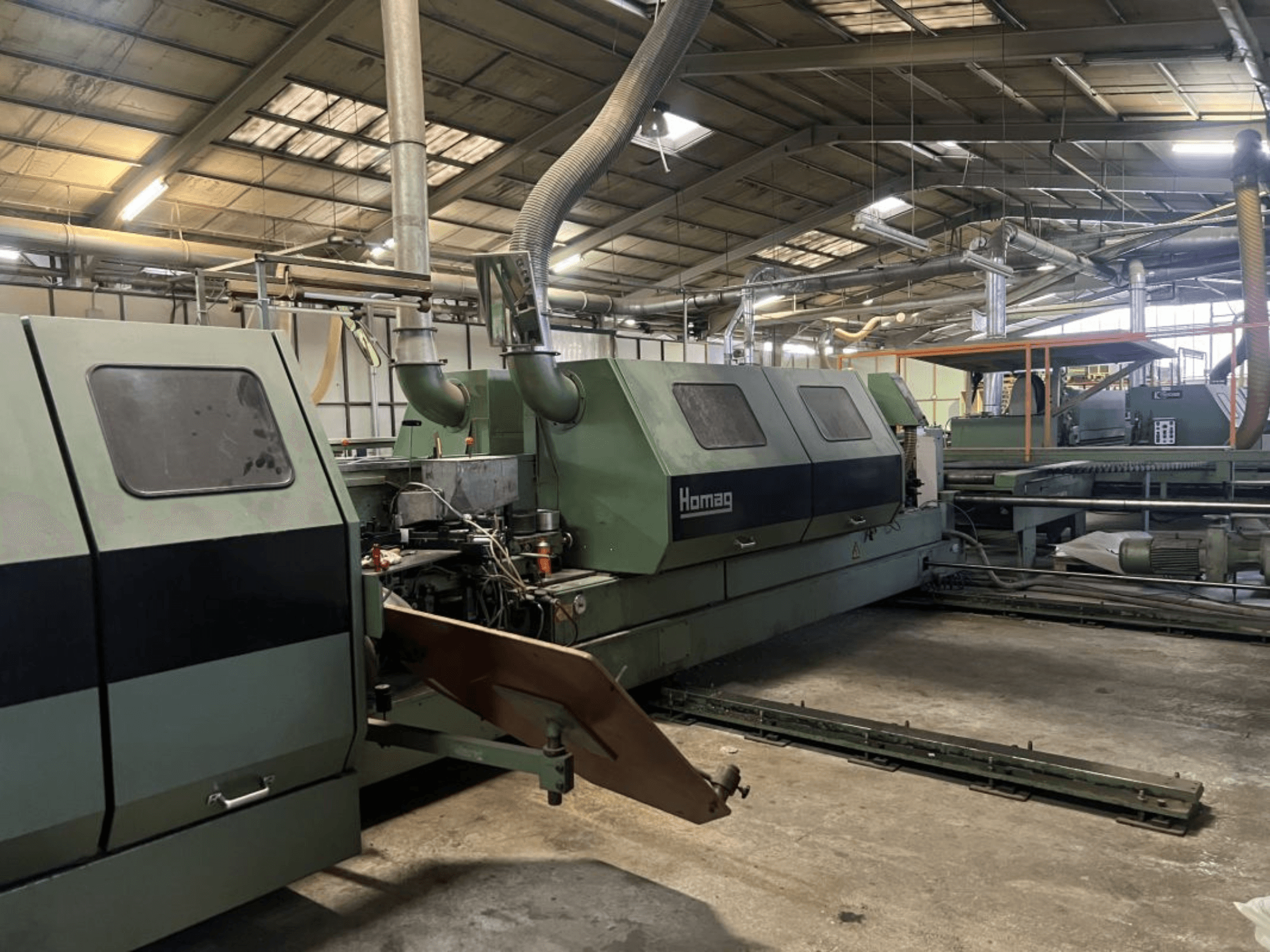 Maszyna przemysłowa Homag w kolorze zielonym, widok z boku, z widocznymi komponentami operacyjnymi i panelem sterowania w otoczeniu magazynu.