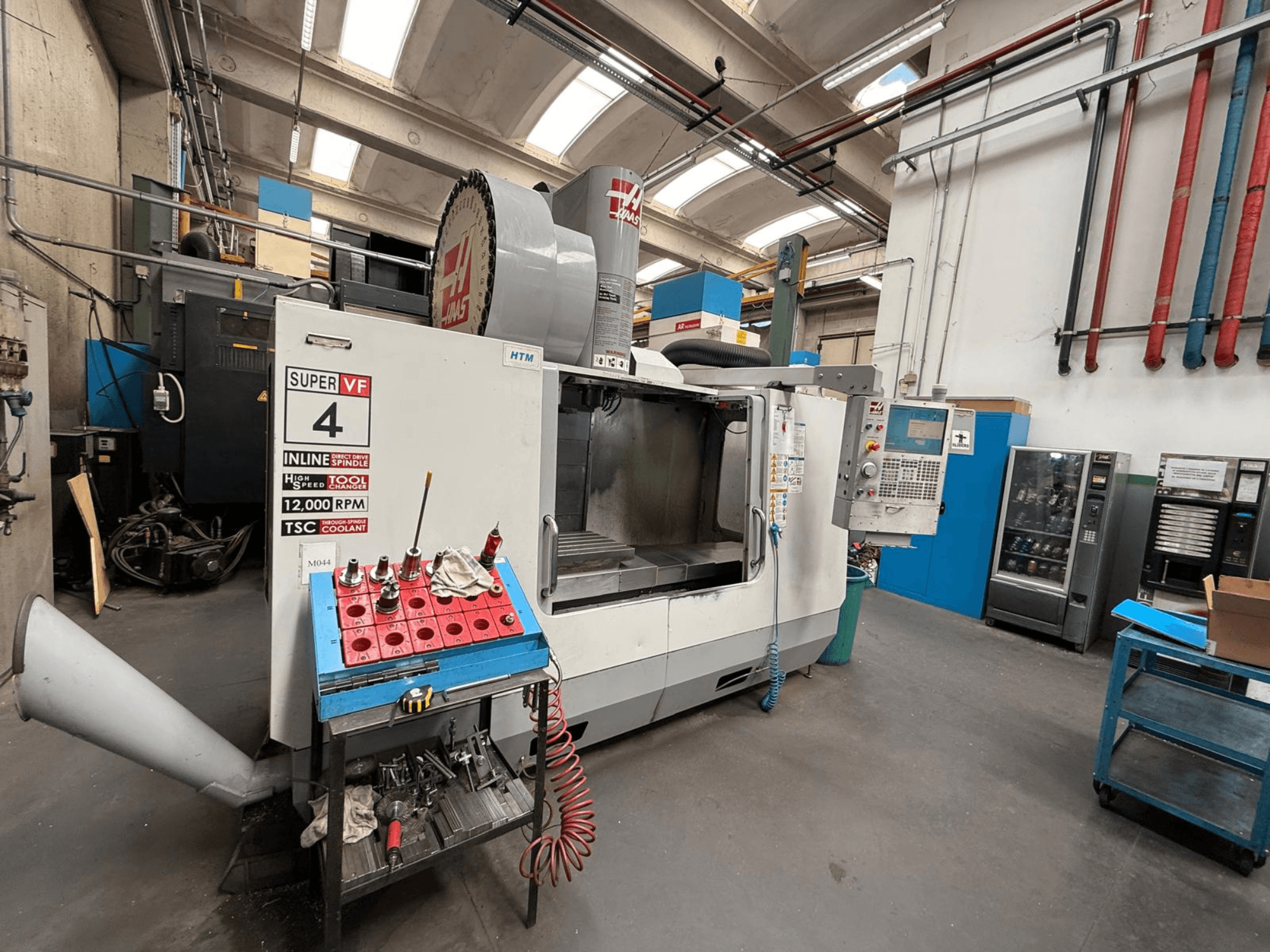 Frezarka CNC HAAS Super VF 4 z panelem sterowania, wrzecionem 12 000 RPM i narzędziami na niebieskim stojaku, widok z boku.