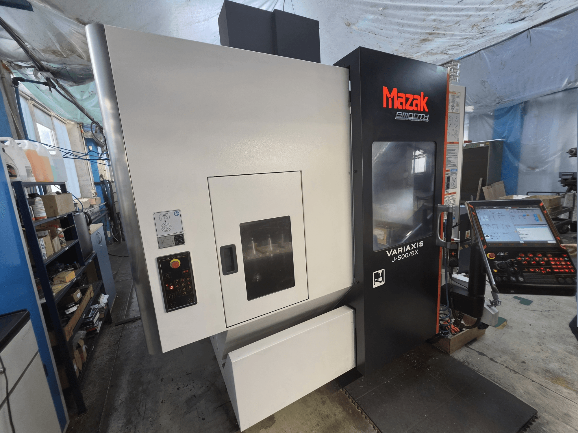 Pionowe centrum obróbcze Mazak VARIAXIS J-500/5X widziane z przodu, wyposażone w panel sterowania i duże okno widokowe na obszar obróbki.