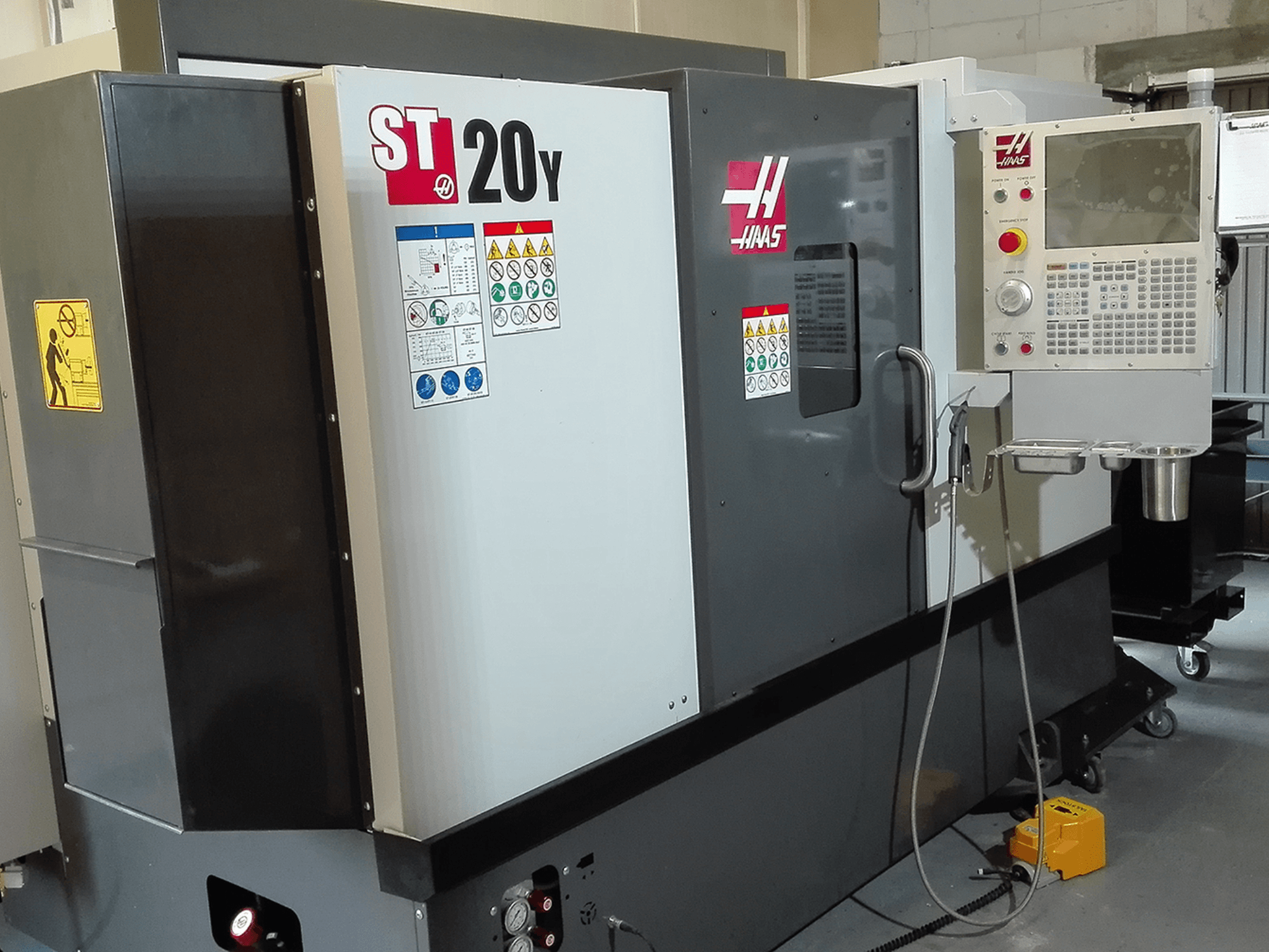 Tokarka CNC Haas ST20Y w widoku z przodu, z panelem sterowania, etykietami bezpieczeństwa i układem chłodzenia.