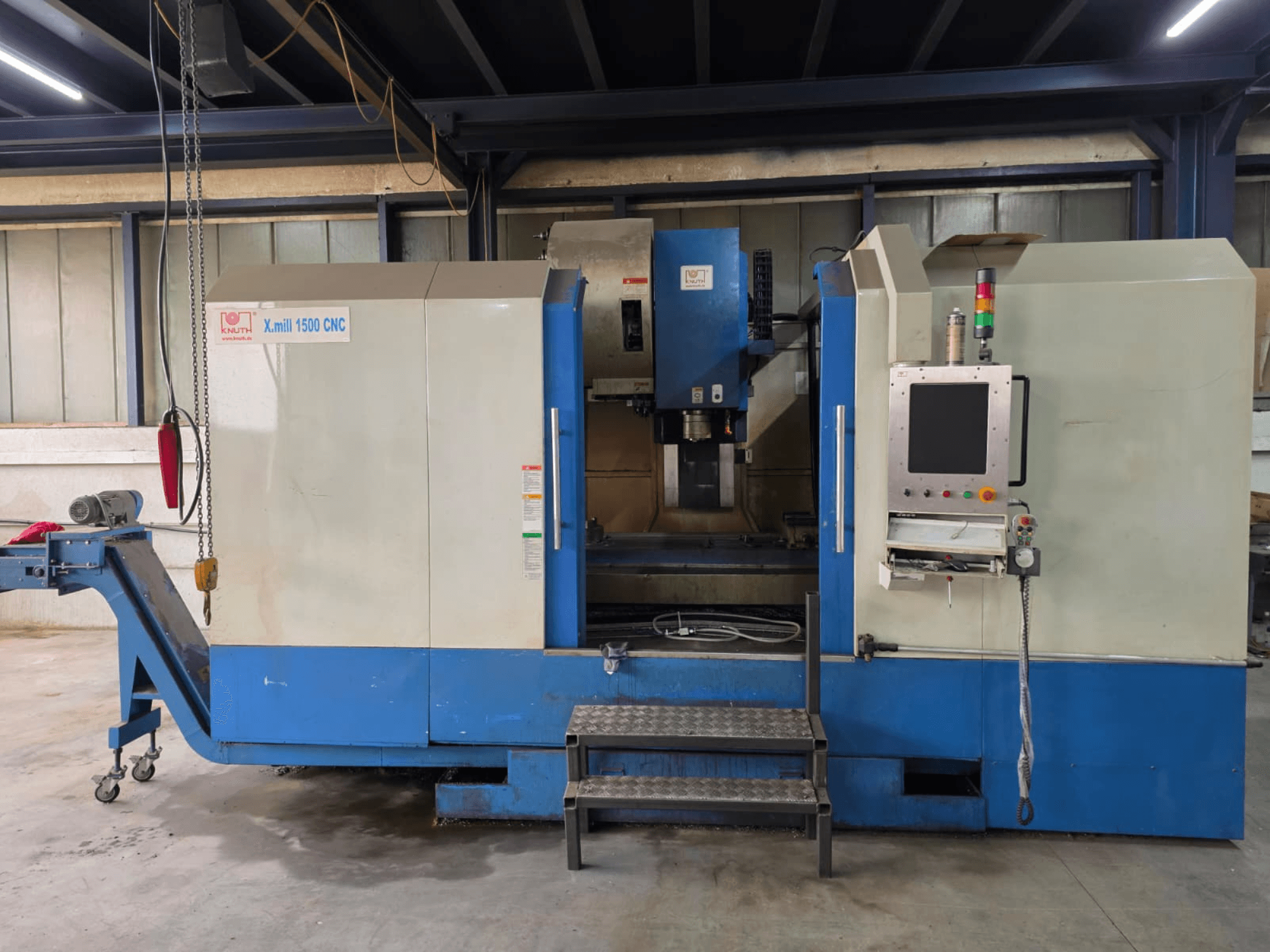 Pionowe centrum obróbcze KNUTH X-MILL 1500 z sterowaniem CNC, widok z boku; widoczny jest panel sterowania, stopnie oraz przenośnik wyjściowy.