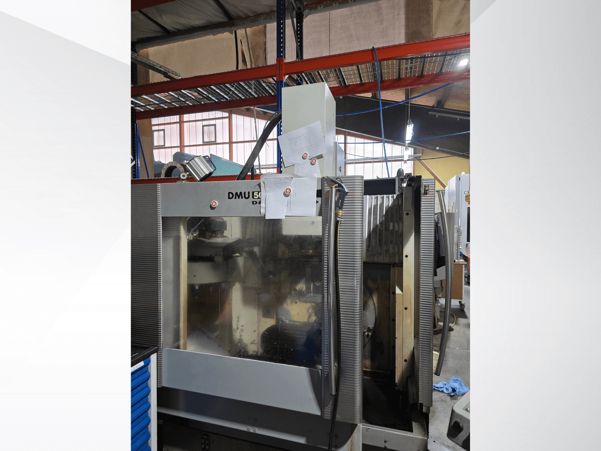3-osiowe centrum obróbcze CNC DMU 50 w warsztacie, pokazane od przodu, z podzespołami roboczymi i załączoną dokumentacją.