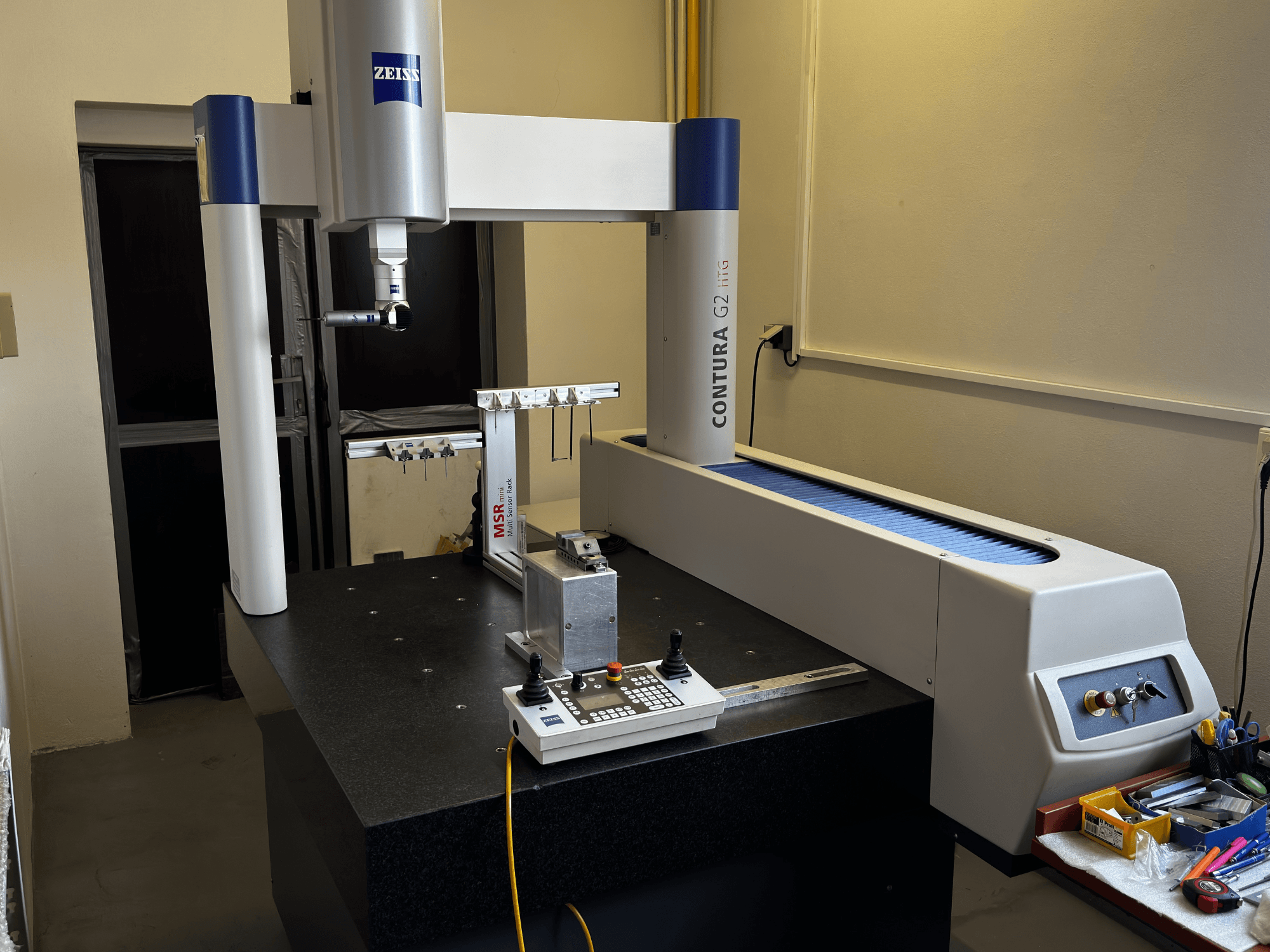 Współrzędnościowa maszyna pomiarowa ZEISS Contura G2 w warunkach laboratoryjnych, widok z przodu przedstawiający ramię pomiarowe, panel sterowania i sąsiednią przestrzeń roboczą.