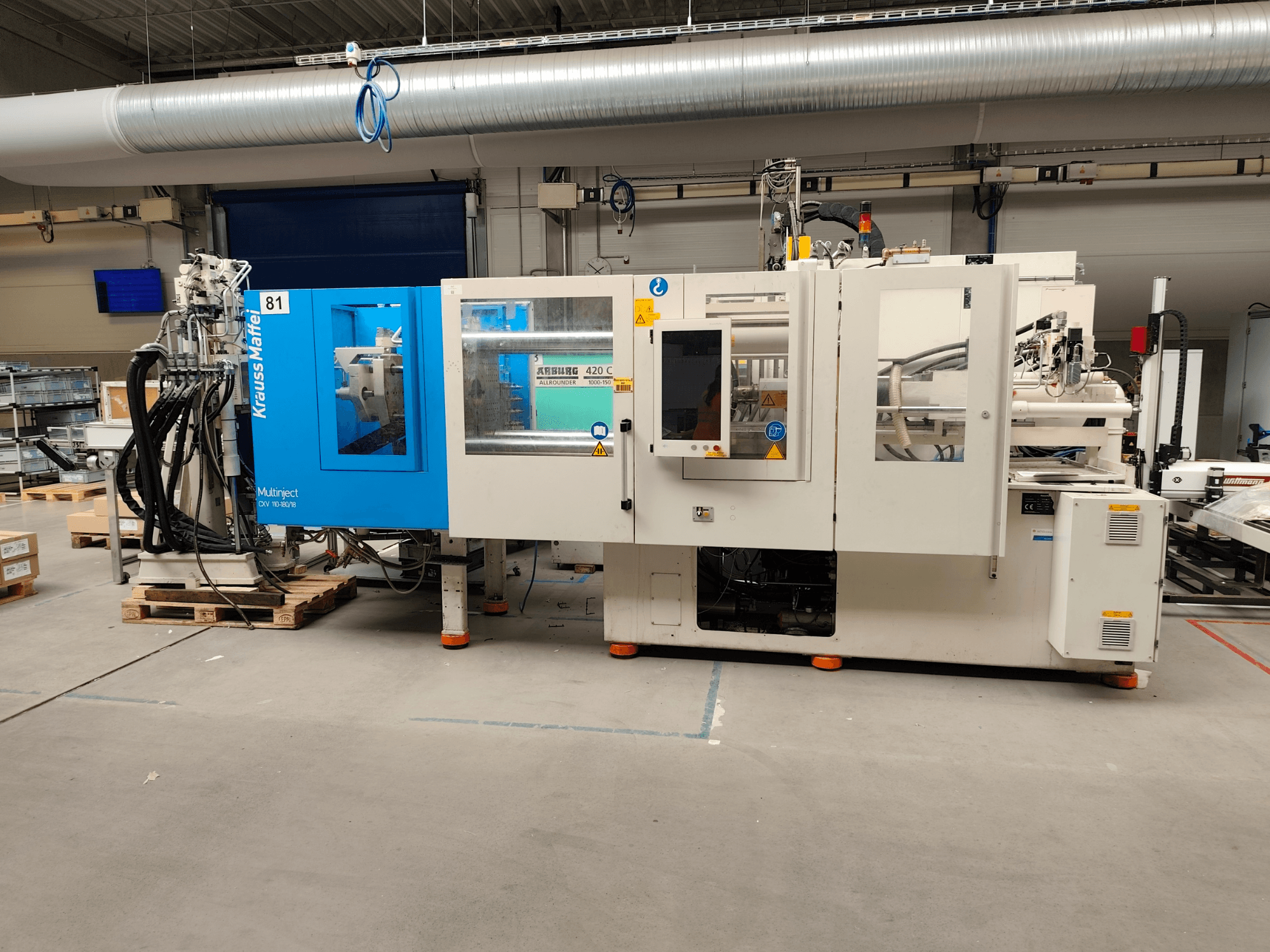 Hydrauliczna wtryskarka Krauss Maffei 110-180-180 CX V, widok z boku, przedstawiająca niebiesko-białą obudowę, panel sterowania oraz złącza.