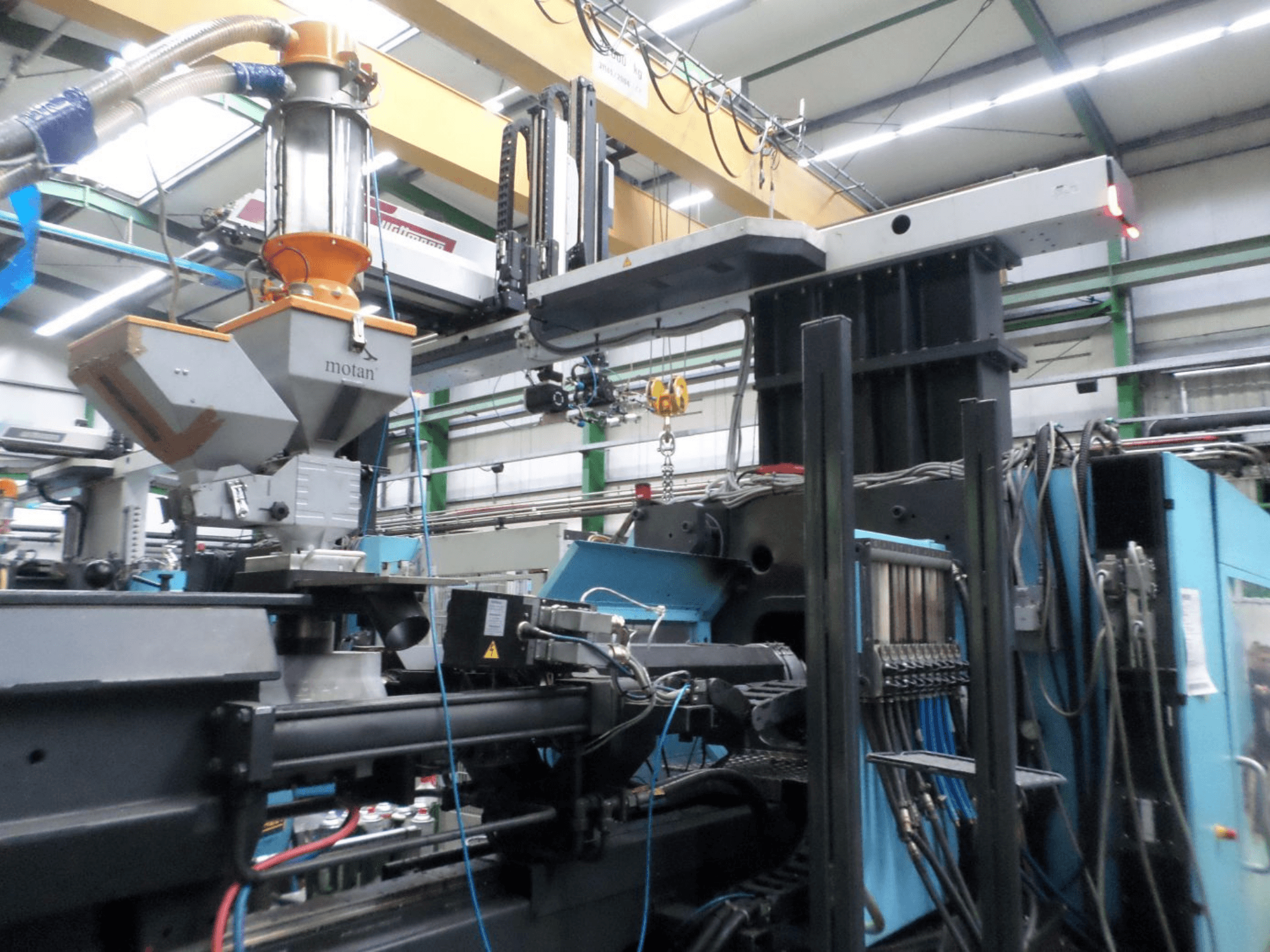 Hydrauliczna wtryskarka DEMAG D 1300, widok z boku, przedstawiająca zbiornik surowca, panel sterowania oraz przyłącza w warunkach fabrycznych.