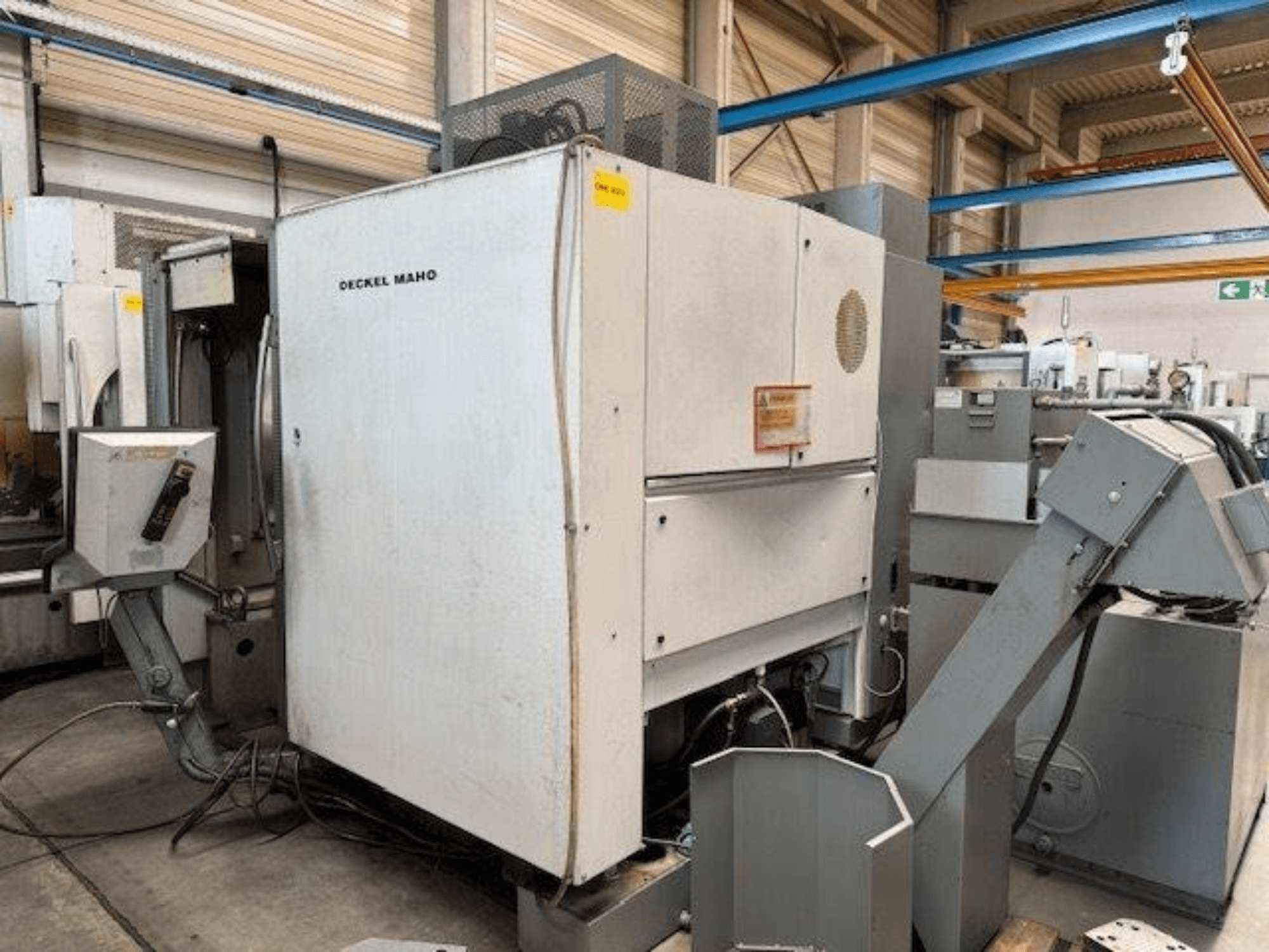Pionowe centrum obróbcze DECKEL MAHO DMC 100 V, widok z boku z widocznym panelem sterowania i różnymi przystawkami.