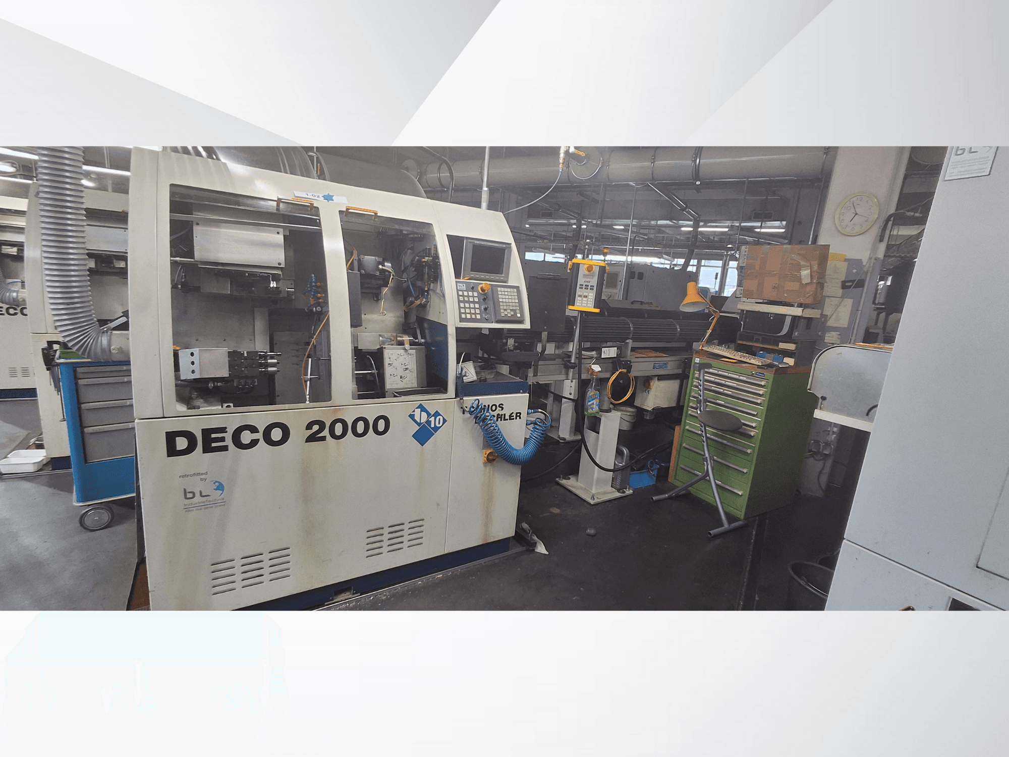 Maszyna DECO 2000 widziana od przodu, z panelem sterowania, rurami i zagraconym obszarem roboczym z narzędziami i skrzynkami.