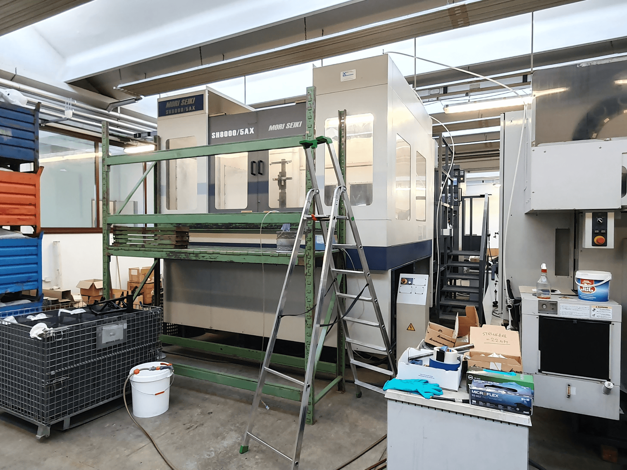 Maszyna CNC Mori Seiki SH-8000/5AX w warsztacie, widok z przodu, z narzędziami warsztatowymi i skrzynkami do przechowywania w pobliżu.