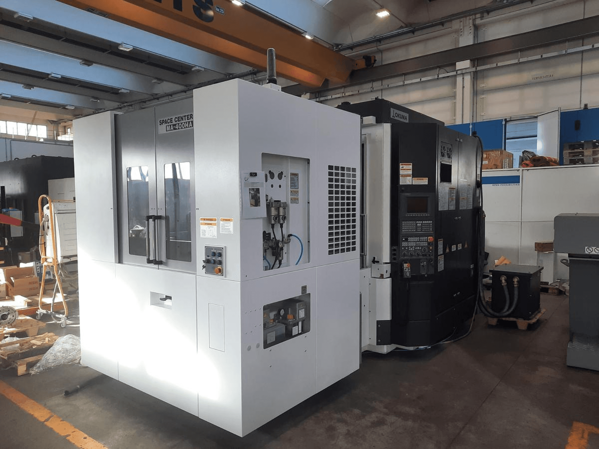 Widok z przodu maszyn CNC SPACE CENTER IM-400HAA i OKUMA z różnymi elementami sterującymi i etykietami producenta.