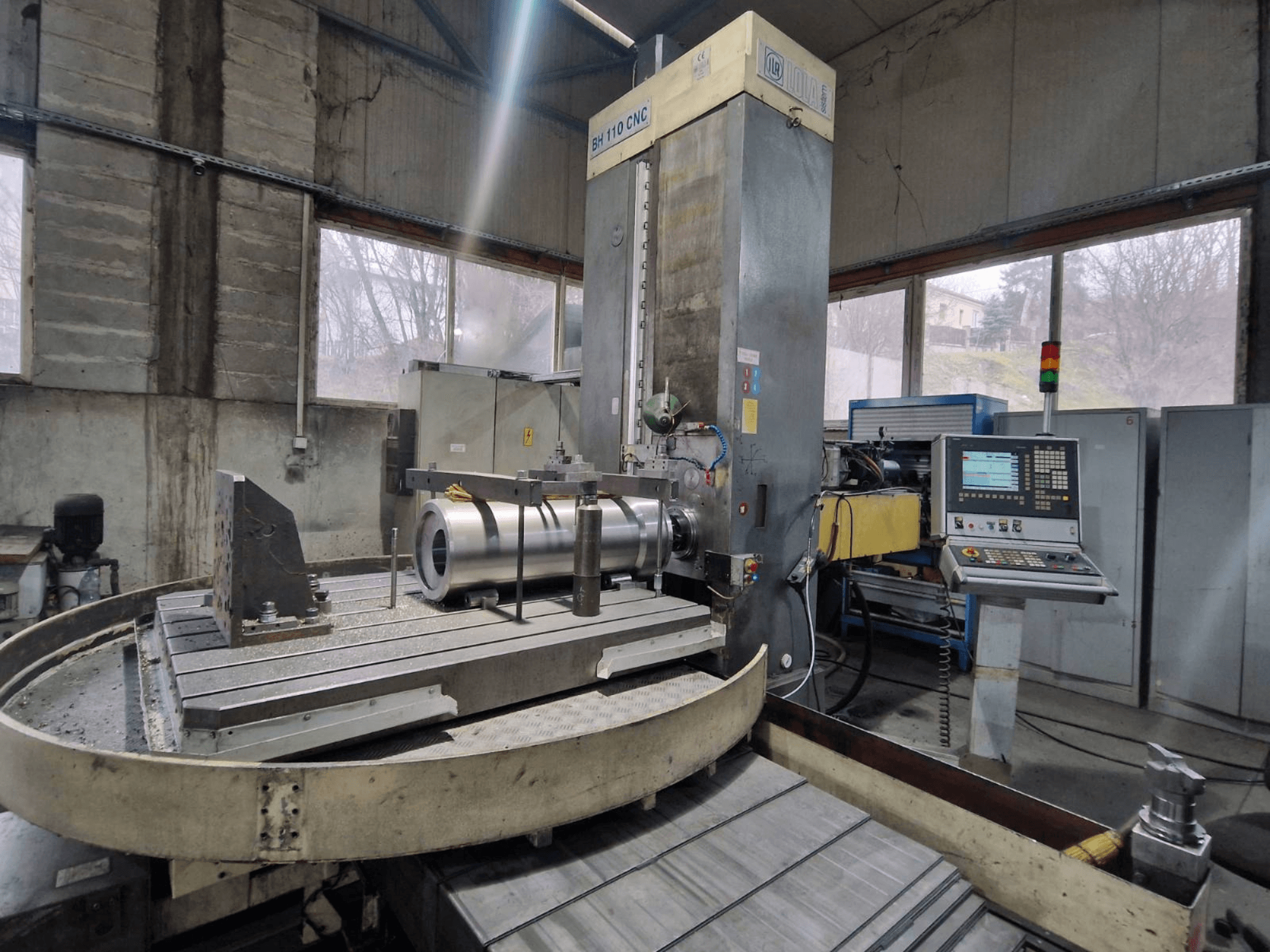 Wytaczarka CNC LOLA BH 110 w warsztacie, widok z przodu, z metalowym przedmiotem obrabianym i panelem sterowania.