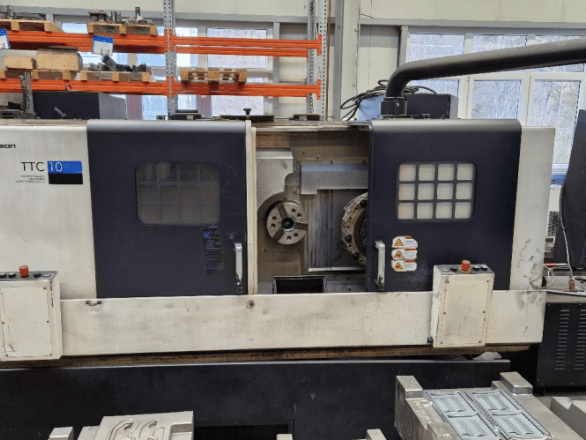 Widok z przodu tokarki TTC 10, pokazujący panel sterowania, widoczne uchwyty i obszar roboczy z metalowymi częściami.