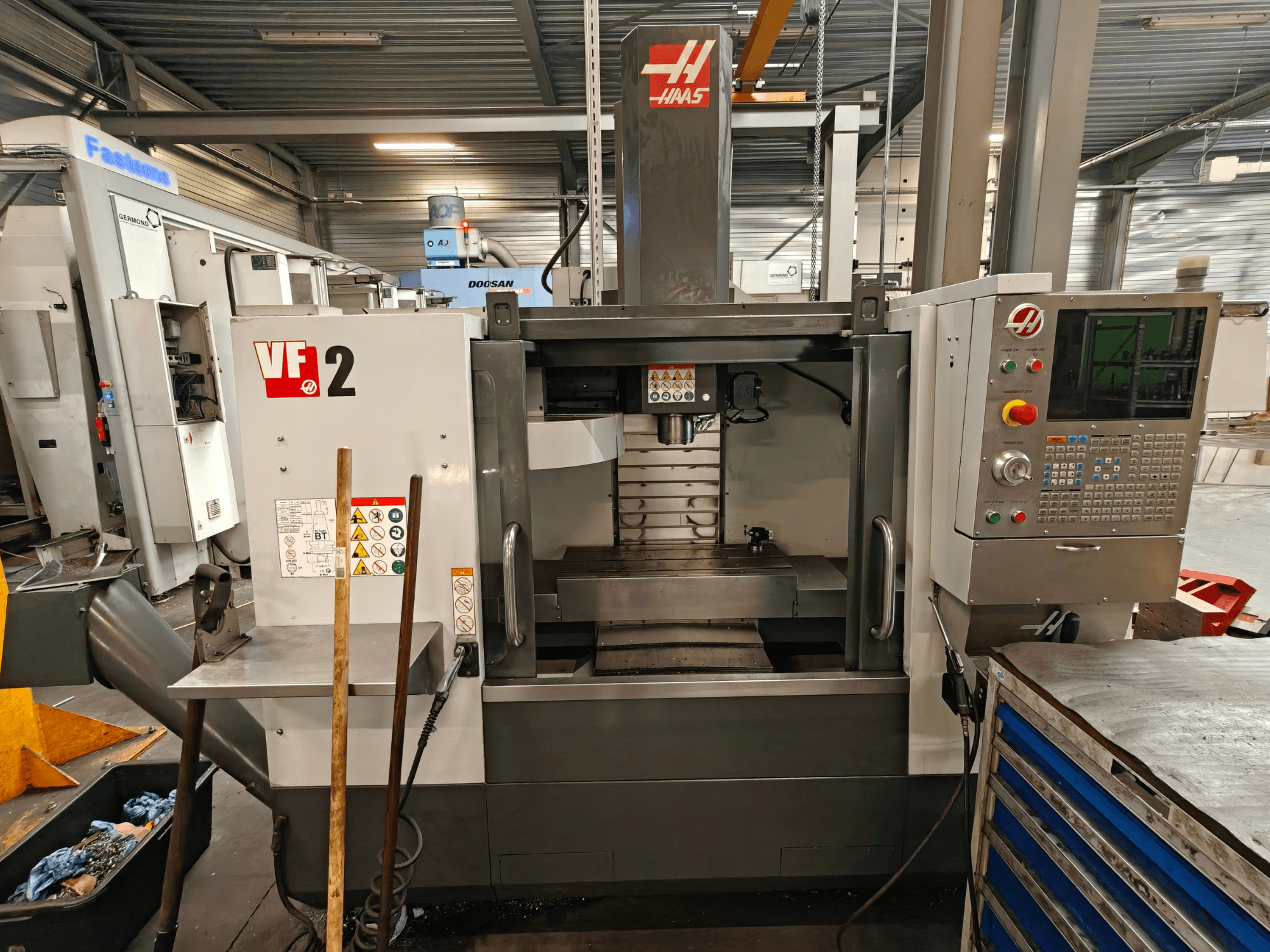 Pionowe centrum obróbcze HAAS VF-2, widok z przodu, przedstawiający elementy sterujące, wrzeciono i stół roboczy w warunkach warsztatowych.