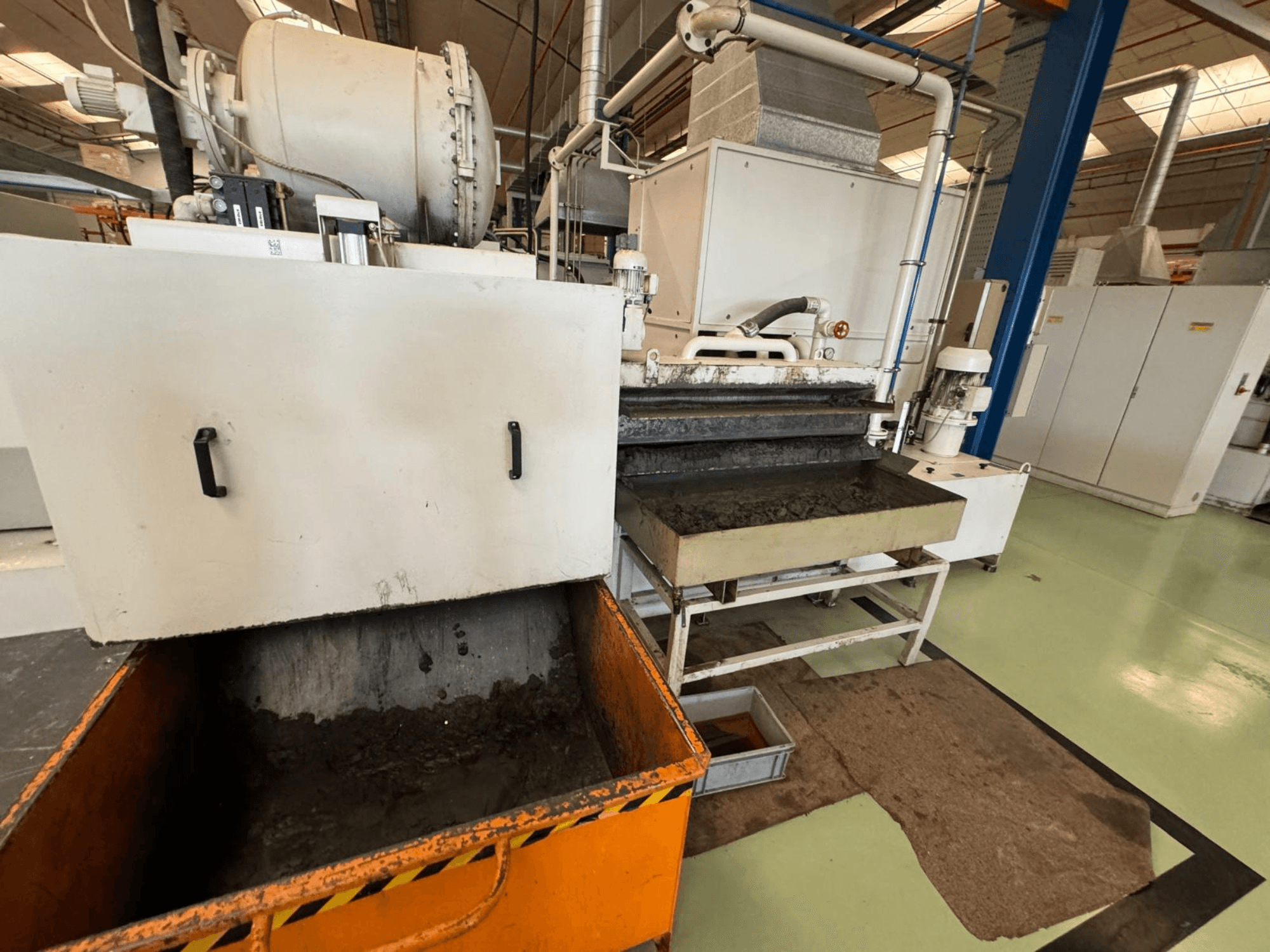 Przemysłowy sprzęt przetwórczy z pomarańczowym pojemnikiem na odpady, widok z przodu; zawiera silnik, przenośniki i obszar konserwacji.