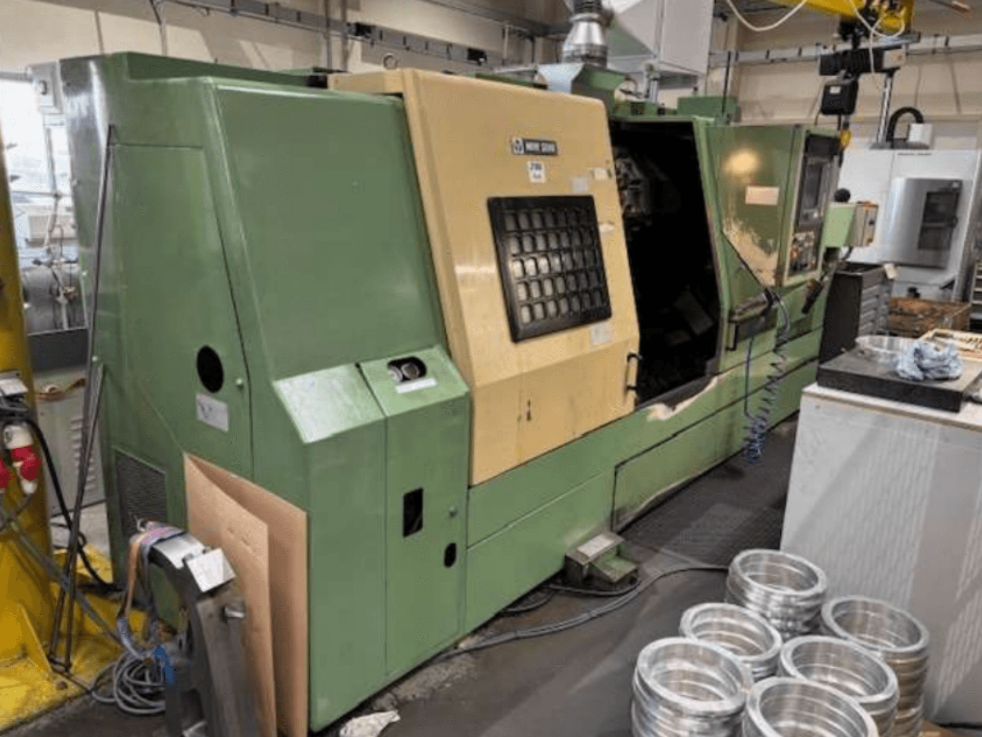 Zielona tokarka CNC firmy Mazak, widziana z przodu, prezentująca panel sterowania i obrabiane części aluminiowe na stole roboczym.