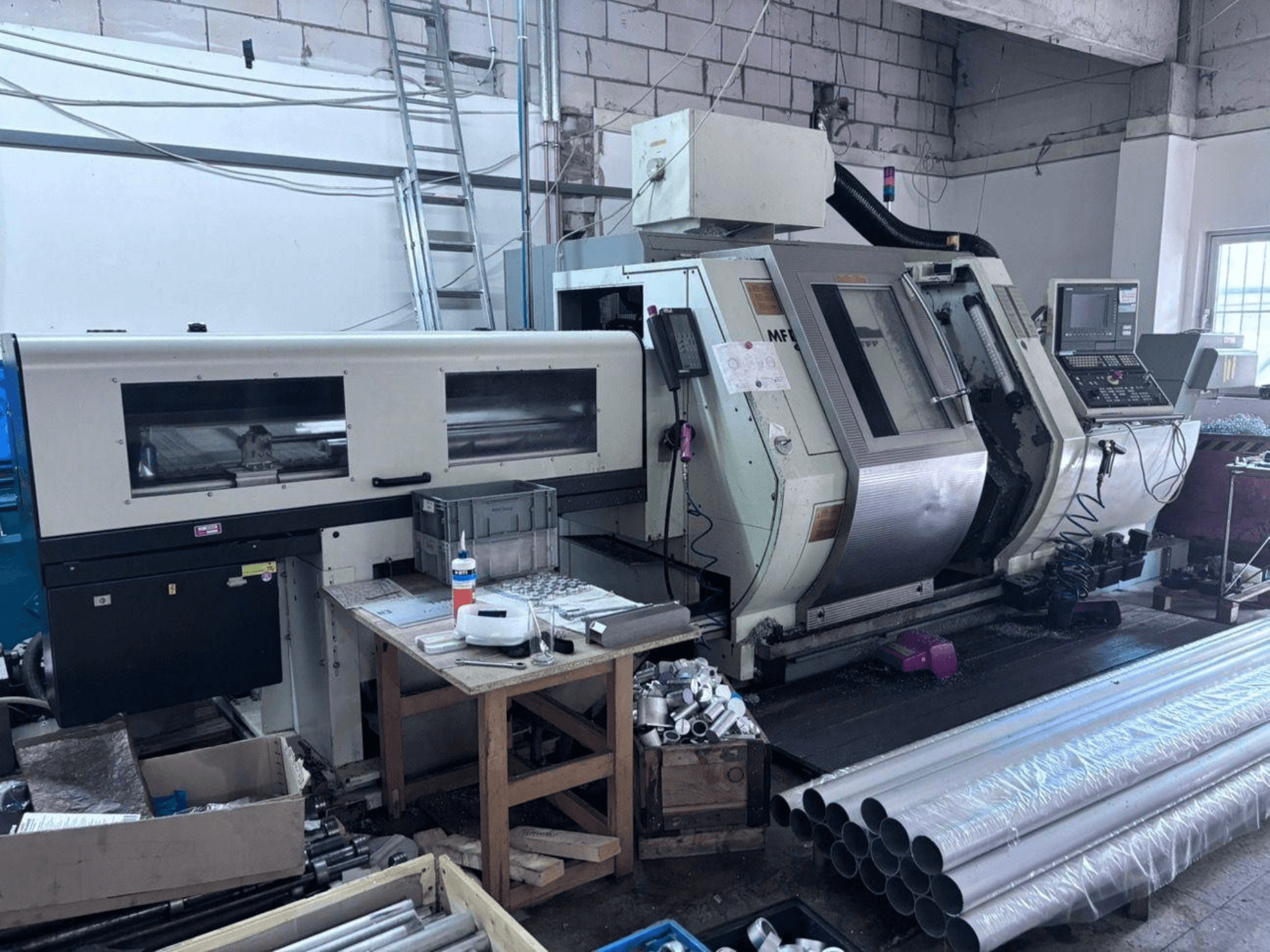 Centrum tokarsko-frezarskie Gildemeister MF Twin 65, widok z boku przedstawiający panel sterowania, obszar obróbki oraz rury aluminiowe.