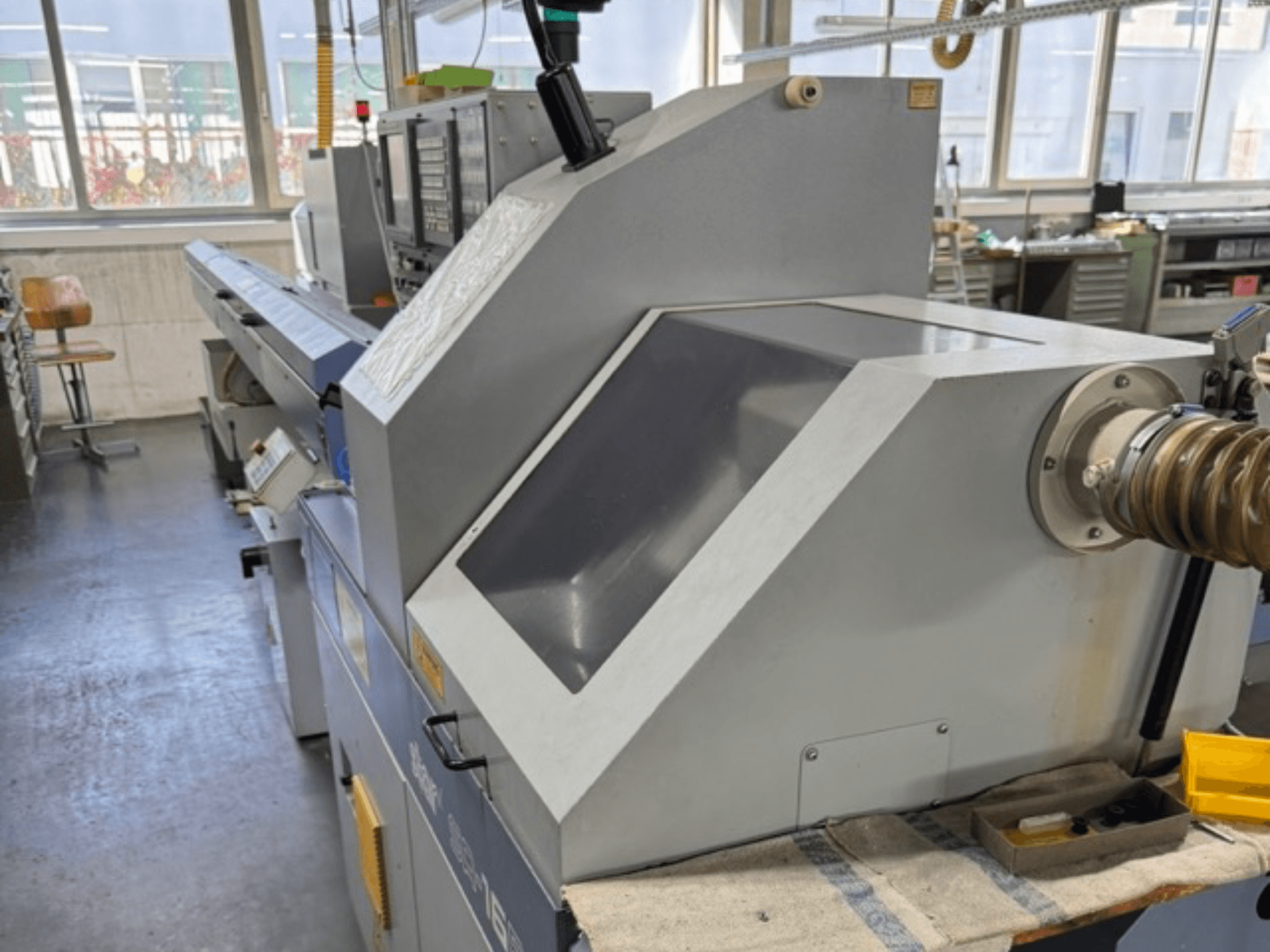 Szara maszyna przemysłowa widziana z boku, posiada duży kątowy panel, przyciski sterujące i mocowanie węża.