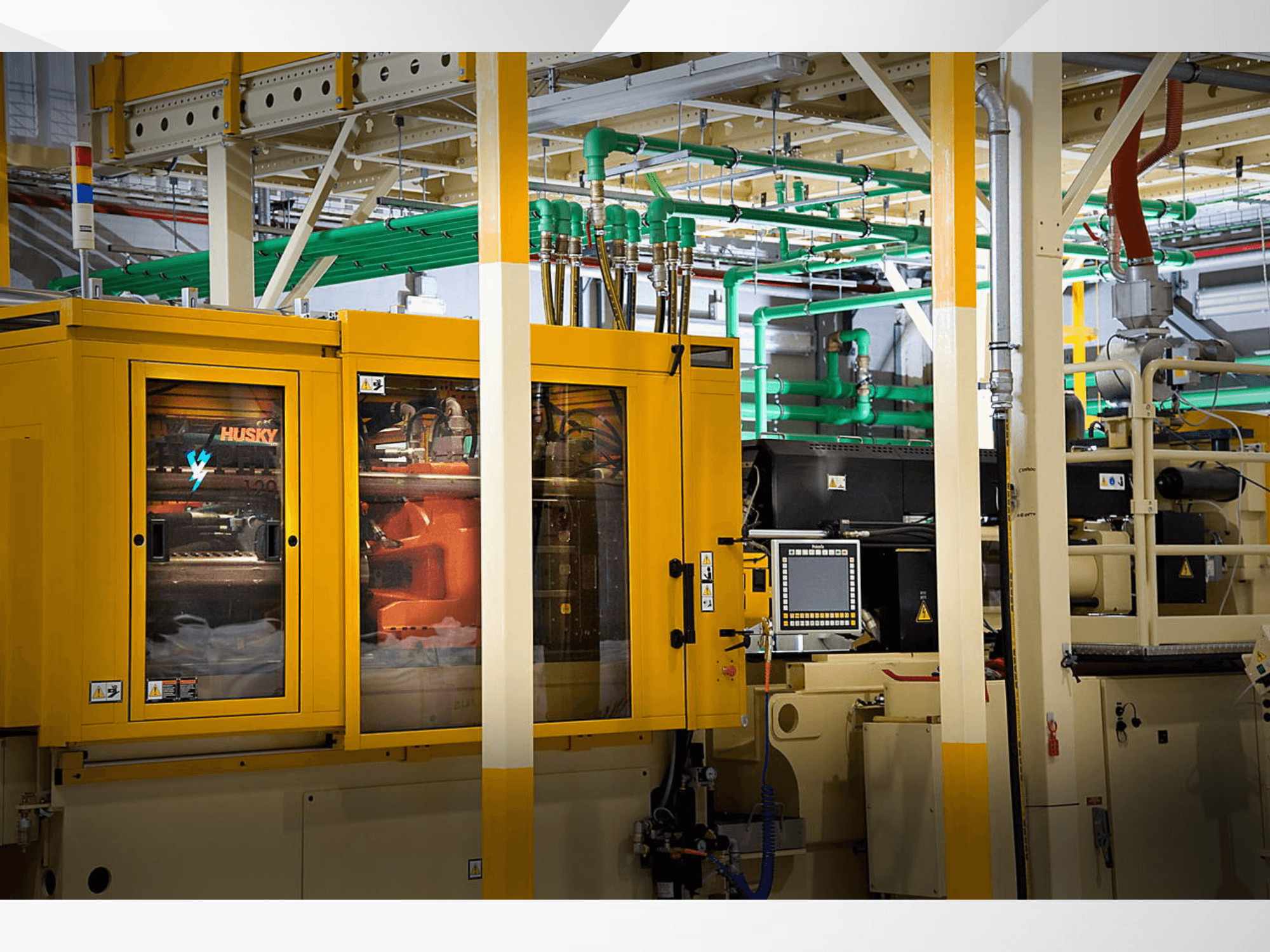 Maszyna przemysłowa Husky w kolorze żółtym, widok z przodu przedstawiający panel sterowania i wewnętrzne mechanizmy na tle fabryki.