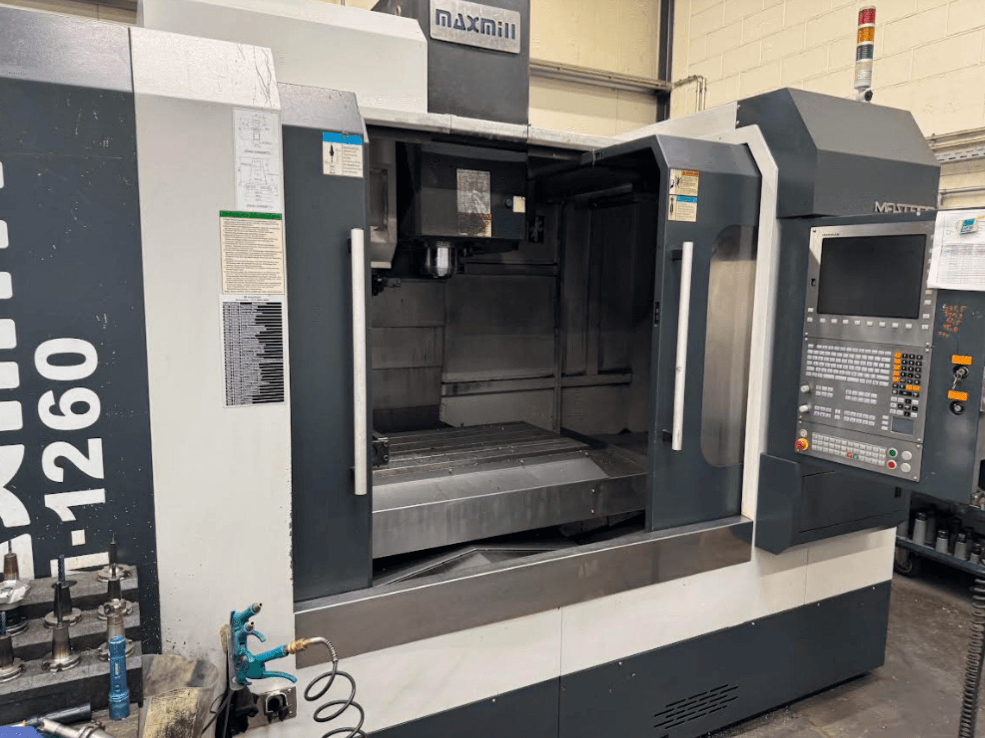 Frezarka CNC Maxmill, model M-1260, widok z przodu przedstawiający pusty obszar roboczy z panelem sterowania i instrukcją obsługi.