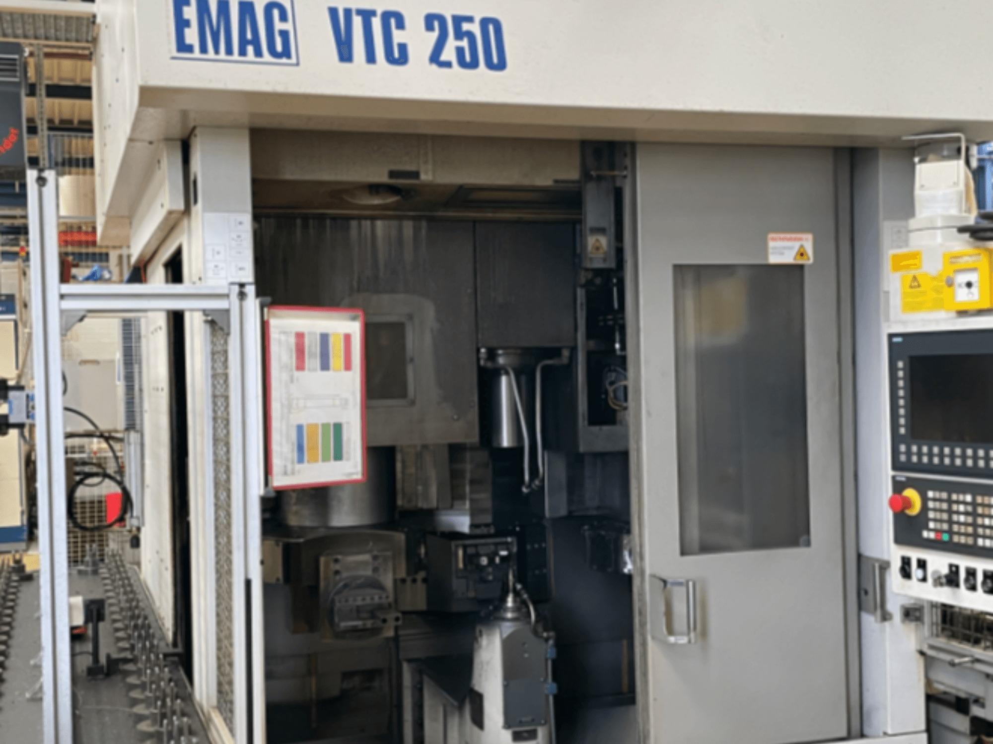Widok z przodu pionowej tokarki EMAG VTC 250, przedstawiający panel sterowania, interfejs operacyjny oraz otwarte drzwiczki dostępowe.