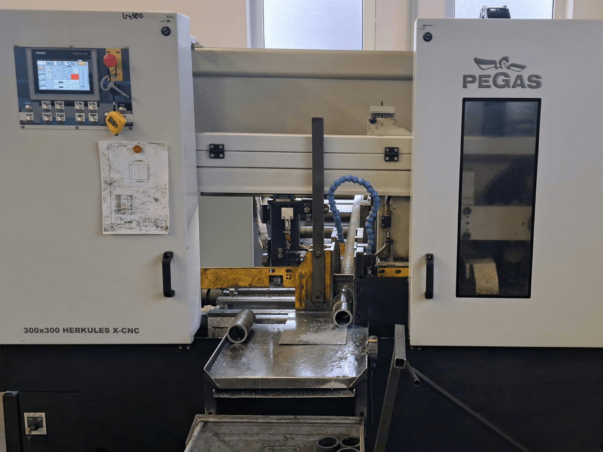 Maszyna do obróbki blachy Pegas HERKULES X-CNC 300x300, widok z przodu, przedstawiający panel sterowania oraz obszar roboczy z elementami metalowymi.