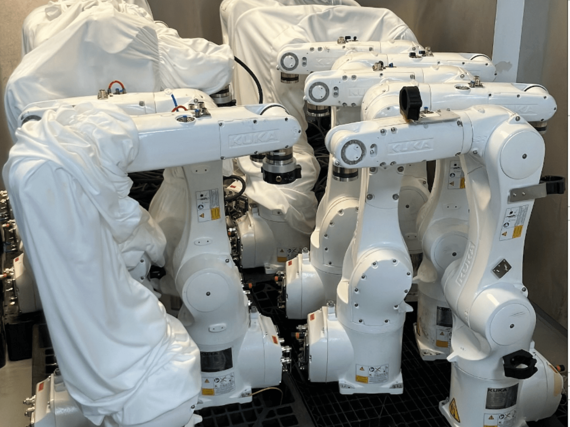 Ramiona robotyczne KUKA KR 10 R900-2 pokryte białą tkaniną, widziane z góry, pokazujące wiele jednostek w magazynie.