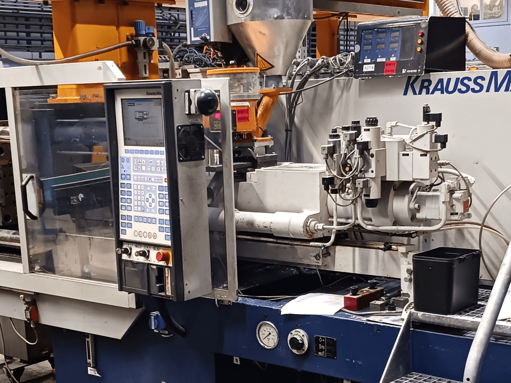 Wtryskarka KraussMaffei z panelem sterowania, jednostkami hydraulicznymi i narzędziami na pierwszym planie, widok z przodu.