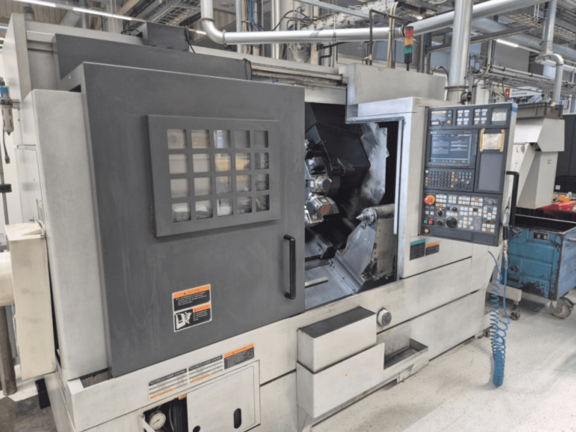 Tokarka CNC z panelem sterowania, widok z przodu. Z widocznym obszarem roboczym i oknem bezpieczeństwa, marka nieznana.