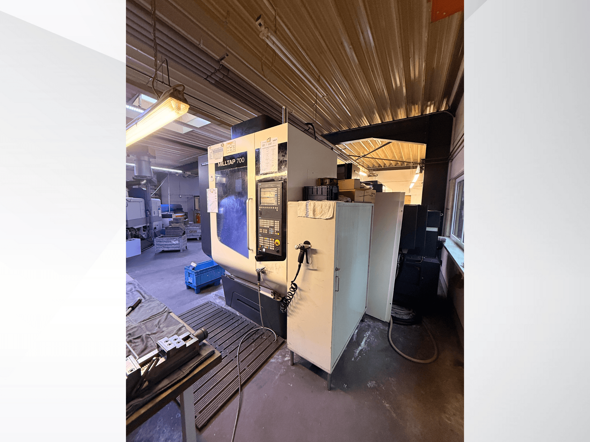 Maszyna CNC Milltap 700 w warsztacie; widok z przodu przedstawia panel sterowania, stojaki na narzędzia i obszary przechowywania z oświetleniem powyżej.