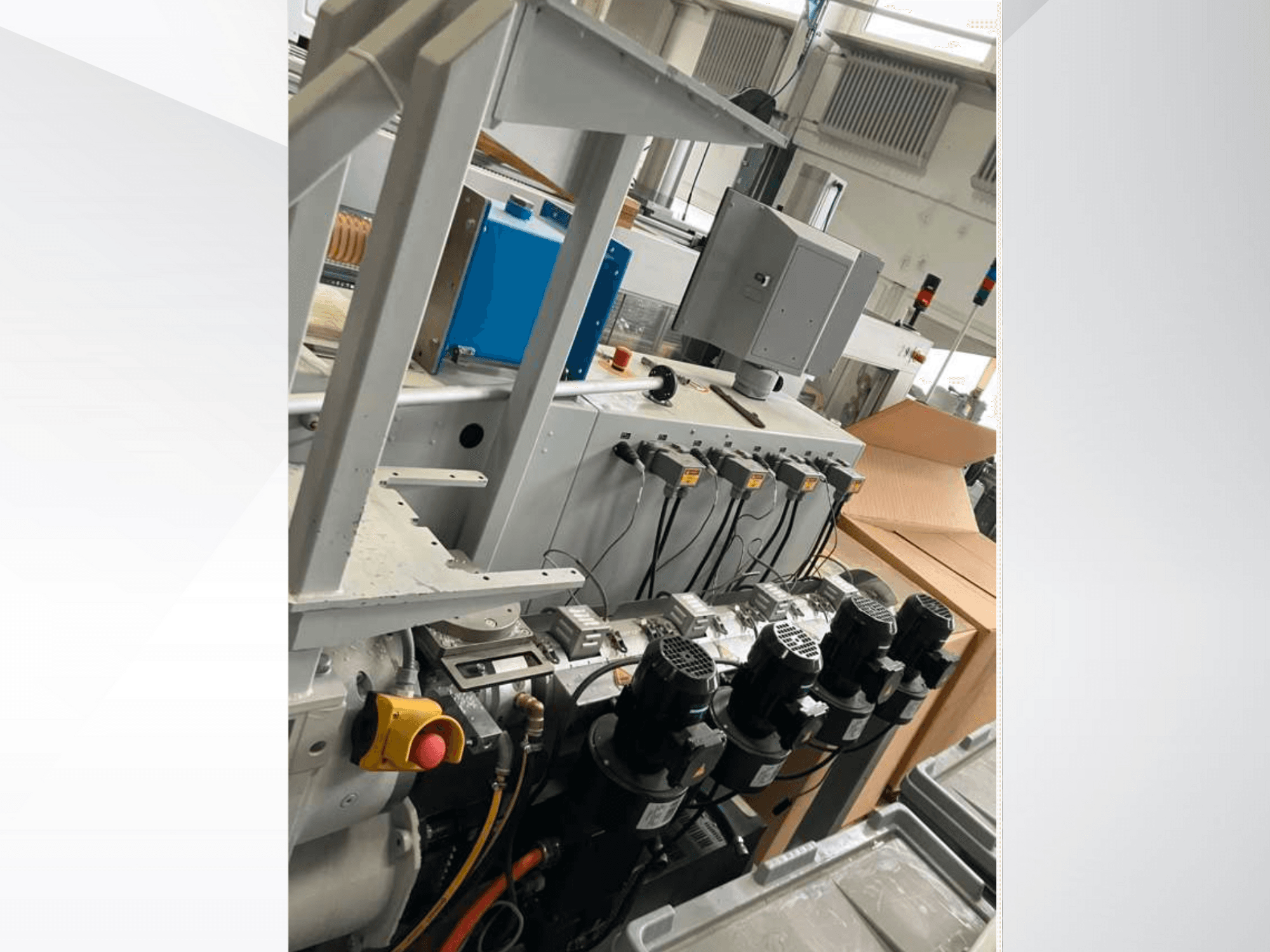 Panel sterowania maszyny przemysłowej z wieloma silnikami, wskaźnikami i monitorem; widok z boku wewnątrz fabryki.