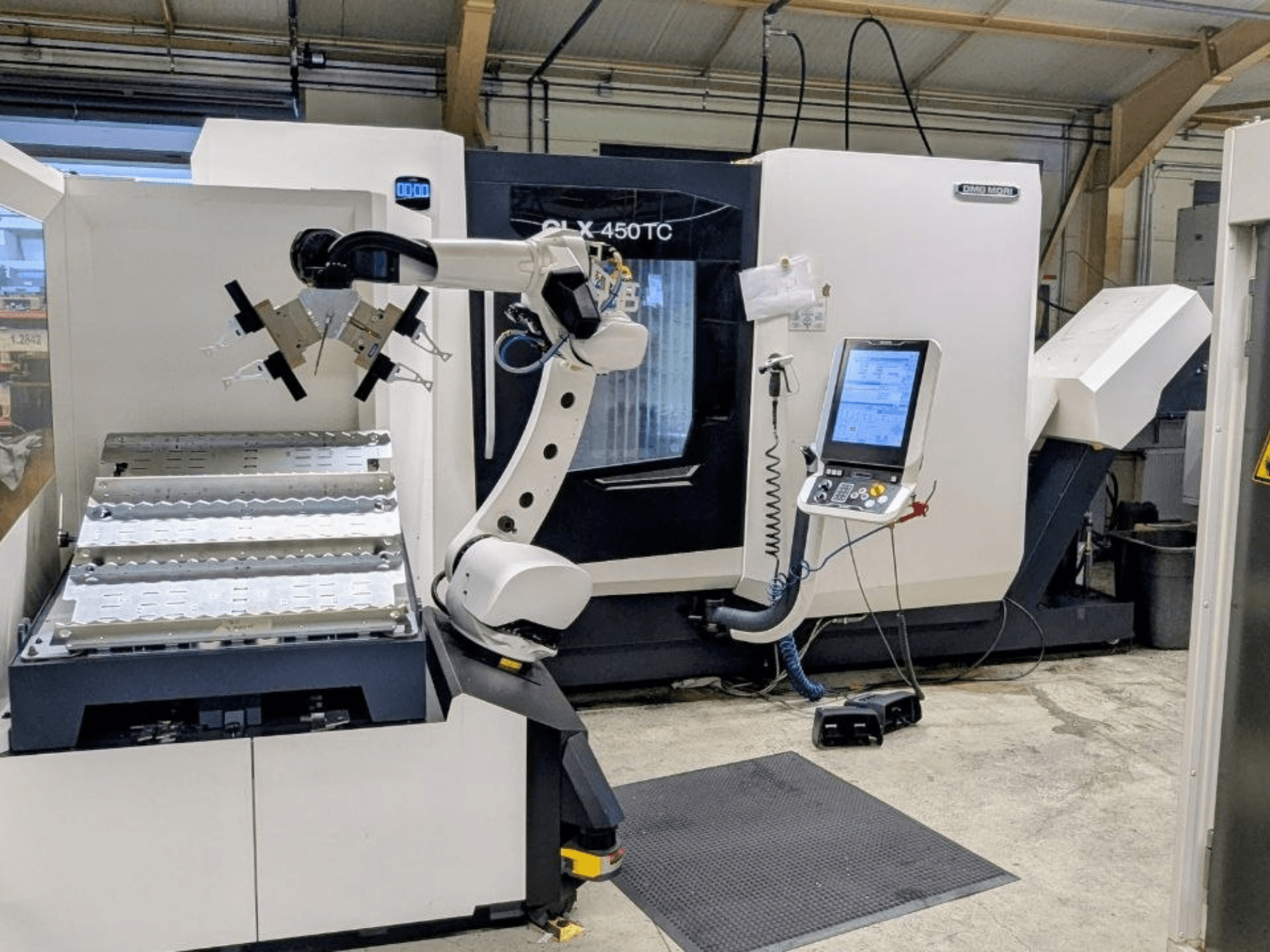 DMG MORI CLX 450 TC z systemem Robo2go, widok z przodu, przedstawiający ramię robota i panel sterowania obok maszyny.