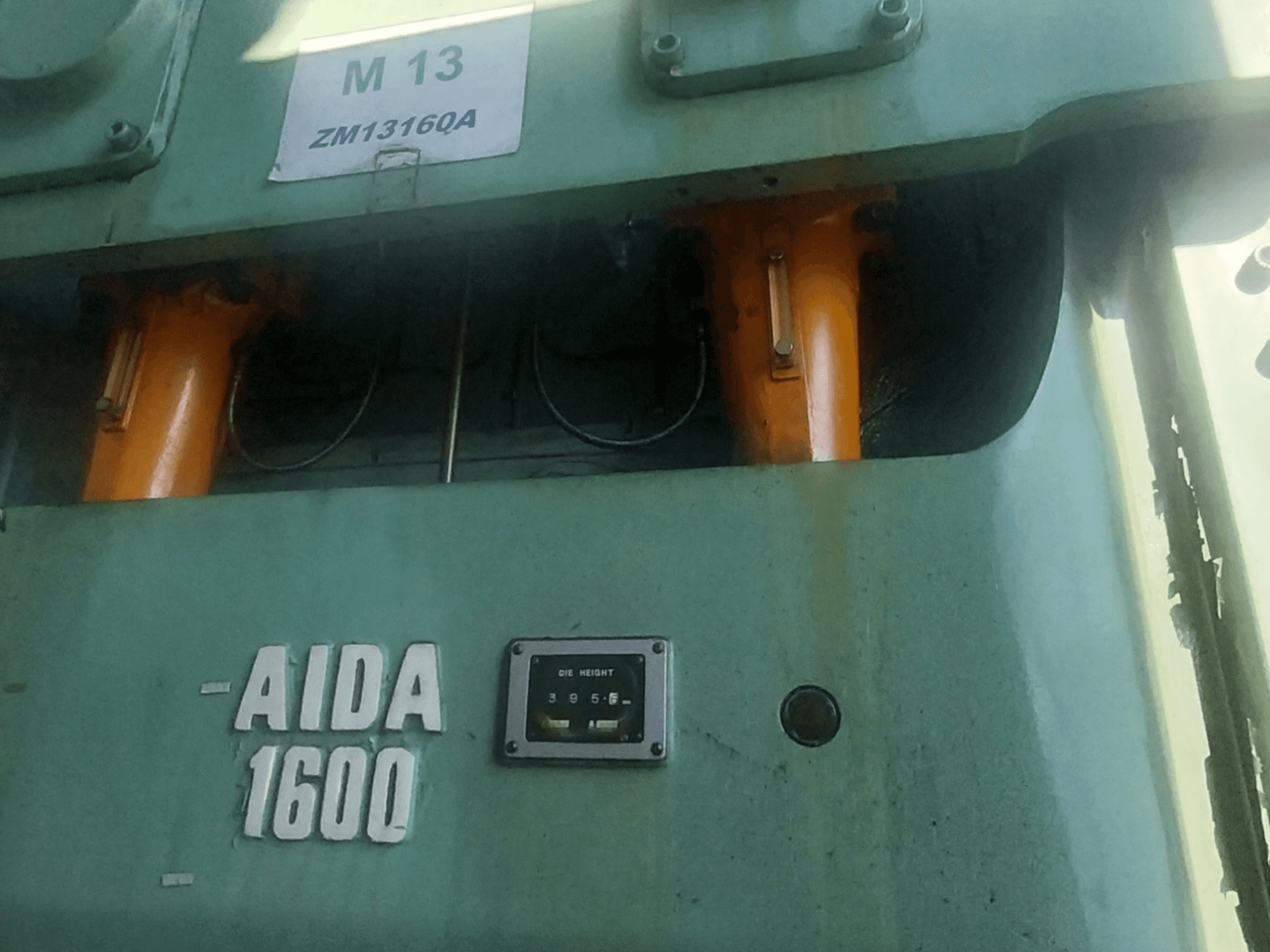 Mechaniczna prasa tłocząca AIDA NC2-1600, widok z przodu; widoczne pomarańczowe elementy hydrauliczne i miernik wysokości matrycy.