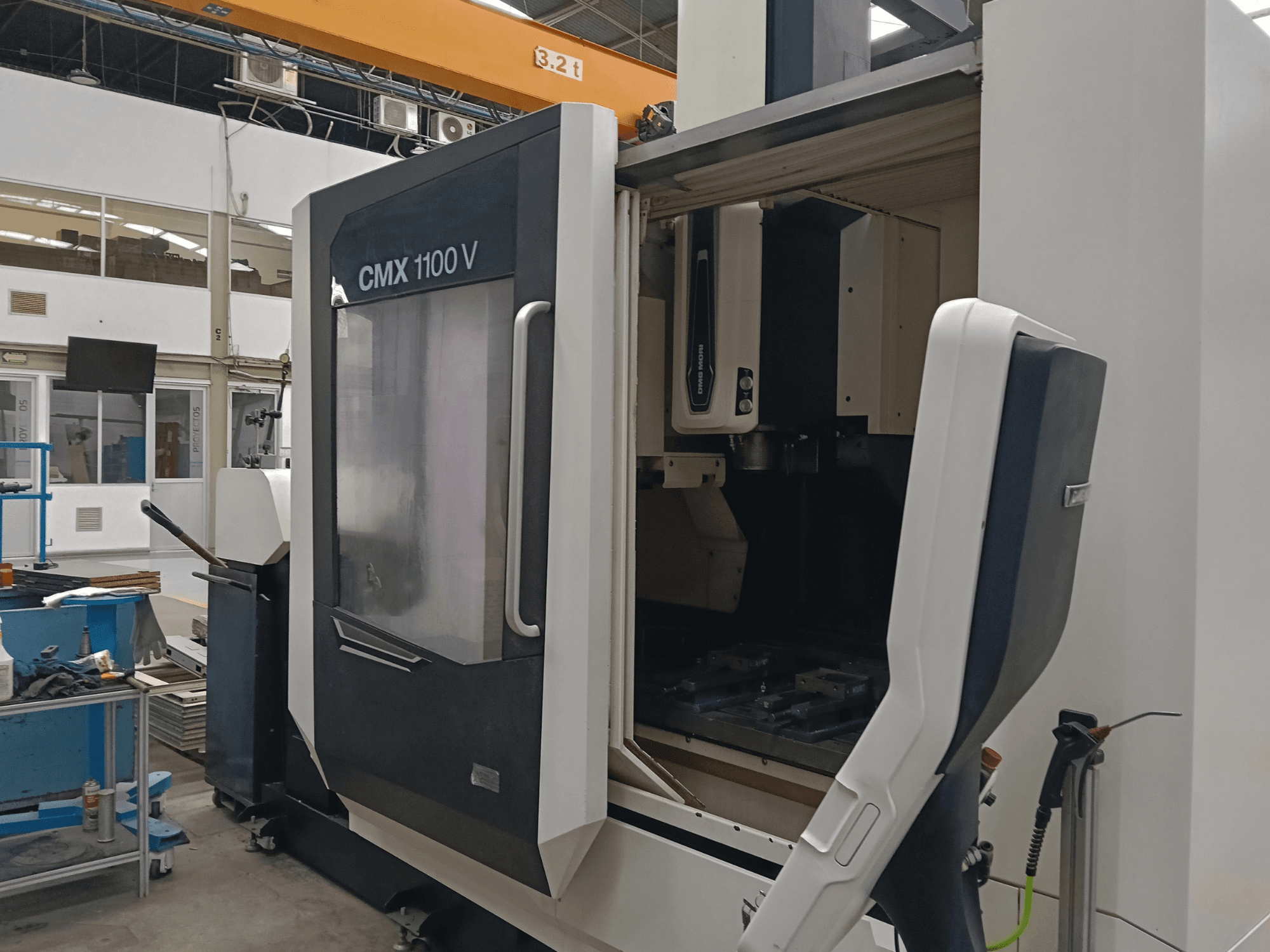 Pionowe centrum obróbcze DMG MORI CMX 1100 V – widok z przodu przedstawiający otwarte drzwiczki oraz układ narzędzi wewnątrz urządzenia w przestrzeni przemysłowej.