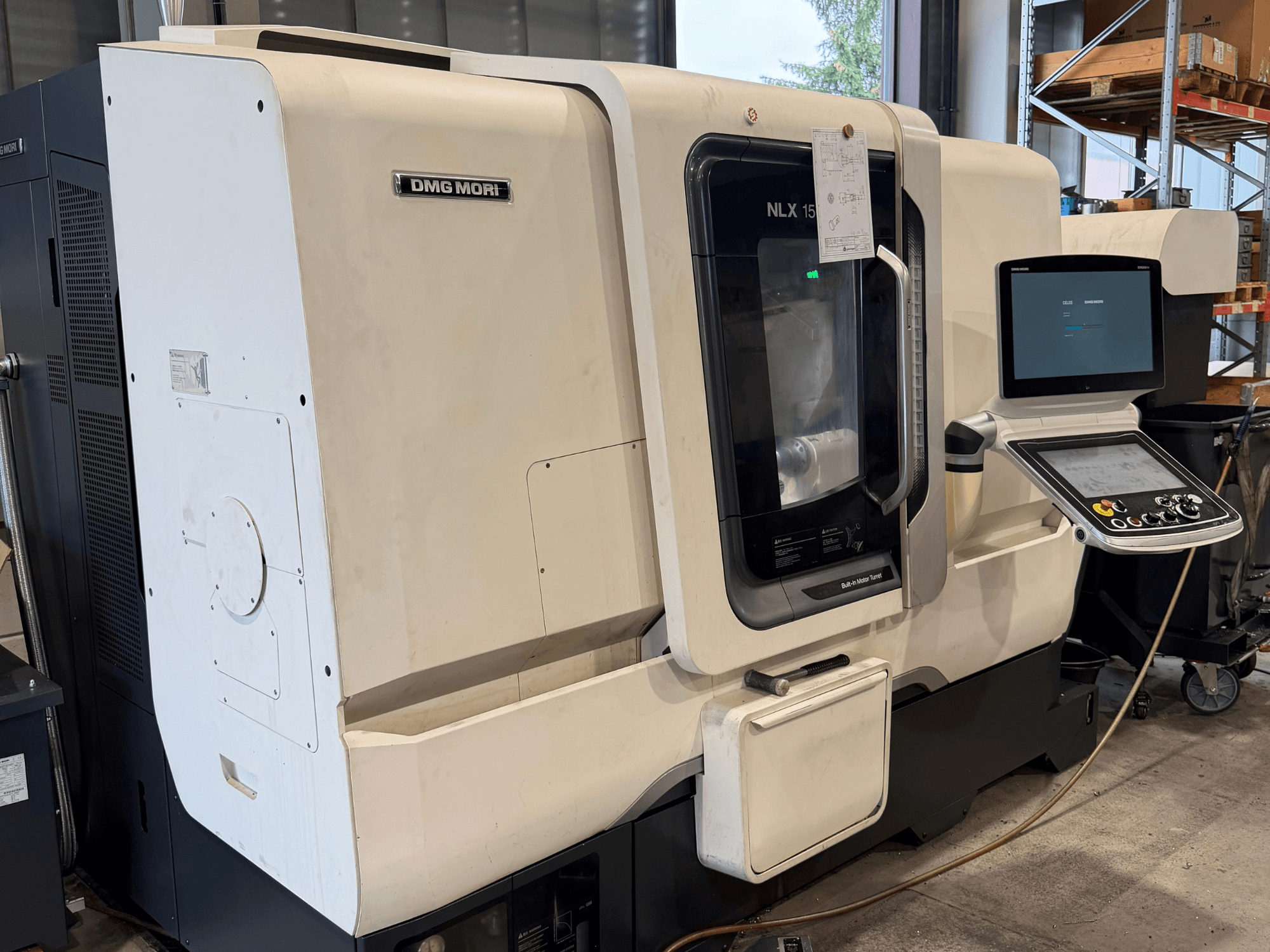 Widok z przodu poziomej tokarki DMG MORI NLX1500MC/500, na którym przez przezroczystą osłonę widać panel sterowania i obszar wrzeciona.