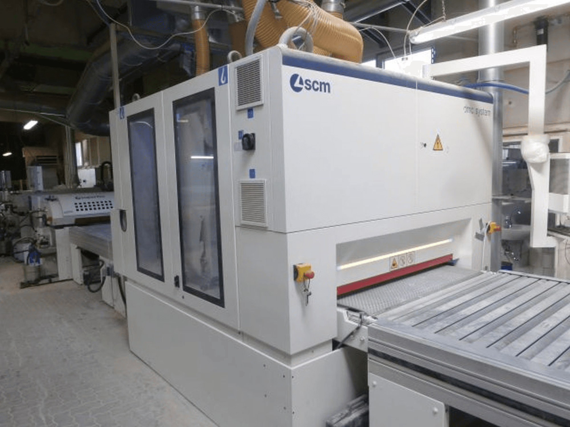 Szlifierka taśmowa SCM DMC SY TC 1350 w warsztacie – widok z boku przedstawiający panel sterowania oraz powierzchnię szlifowania wraz z elementami zabezpieczającymi.