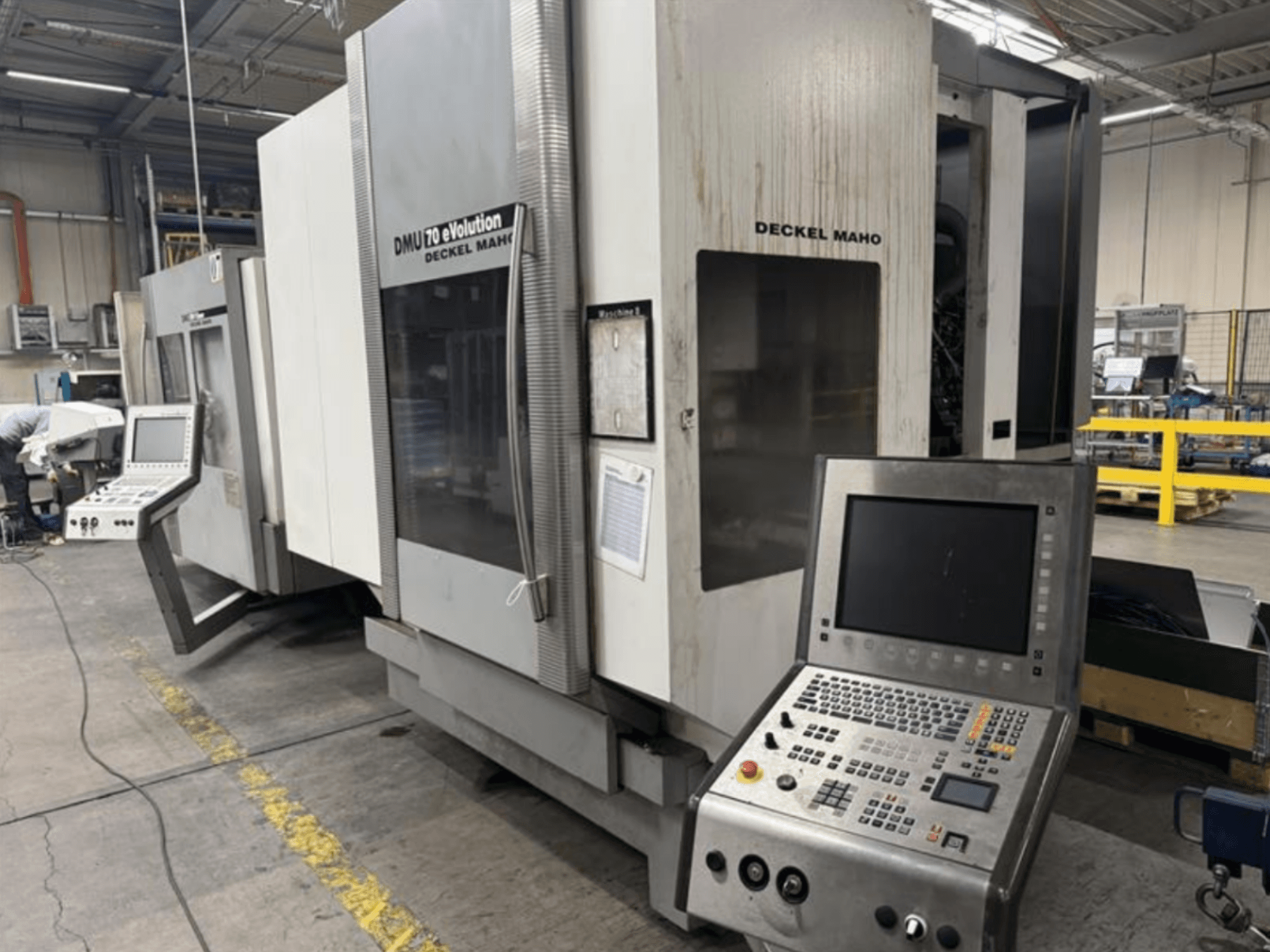 Widok z przodu maszyny CNC Deckel Maho DMU 70 eVOLUTION z panelem sterowania, znajdującej się w zakładzie produkcyjnym.