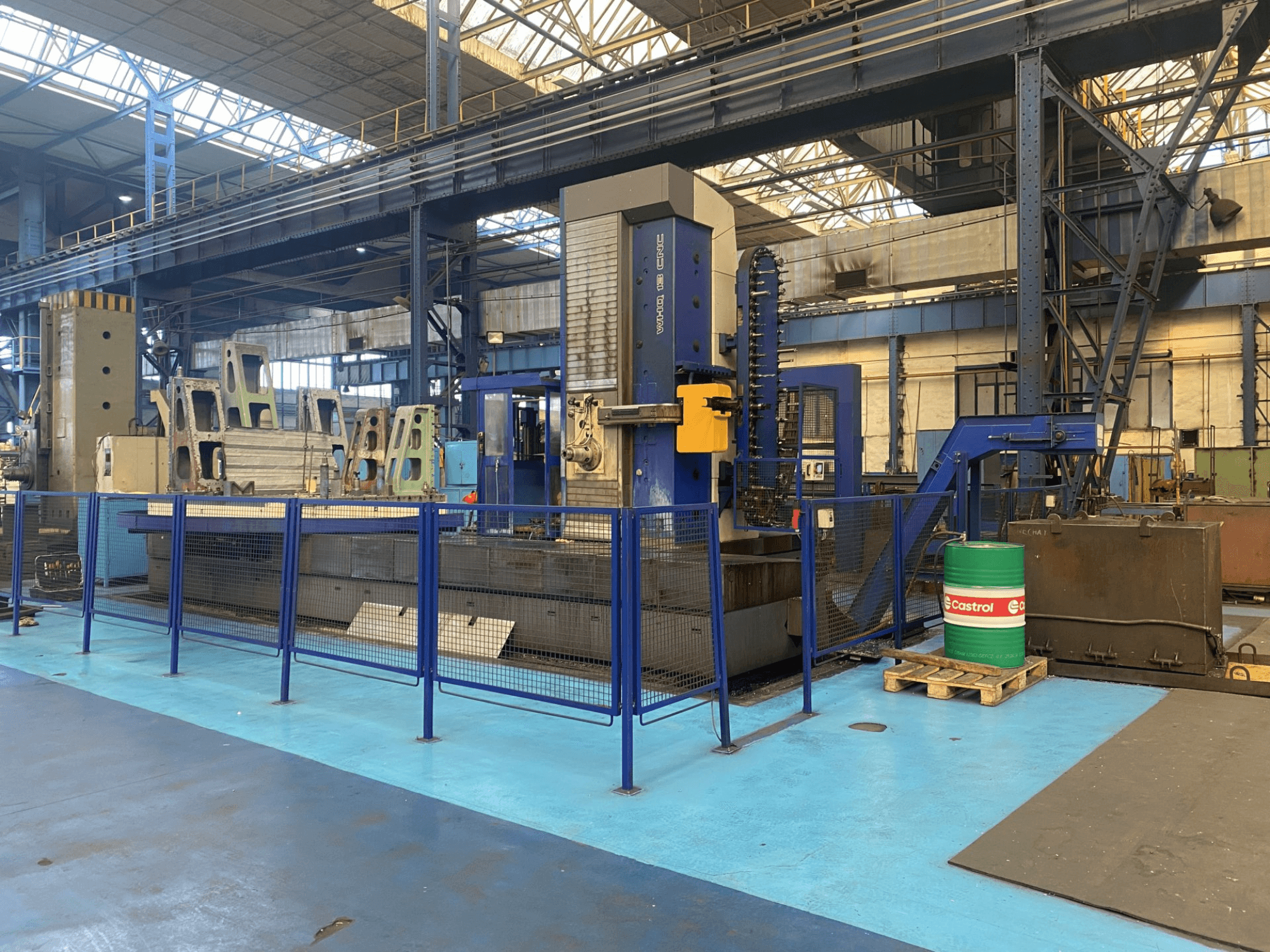 Wytaczarka CNC TOS WHQ 13 w warsztacie, widok z przodu, niebieska rama i otaczające ogrodzenie ochronne.