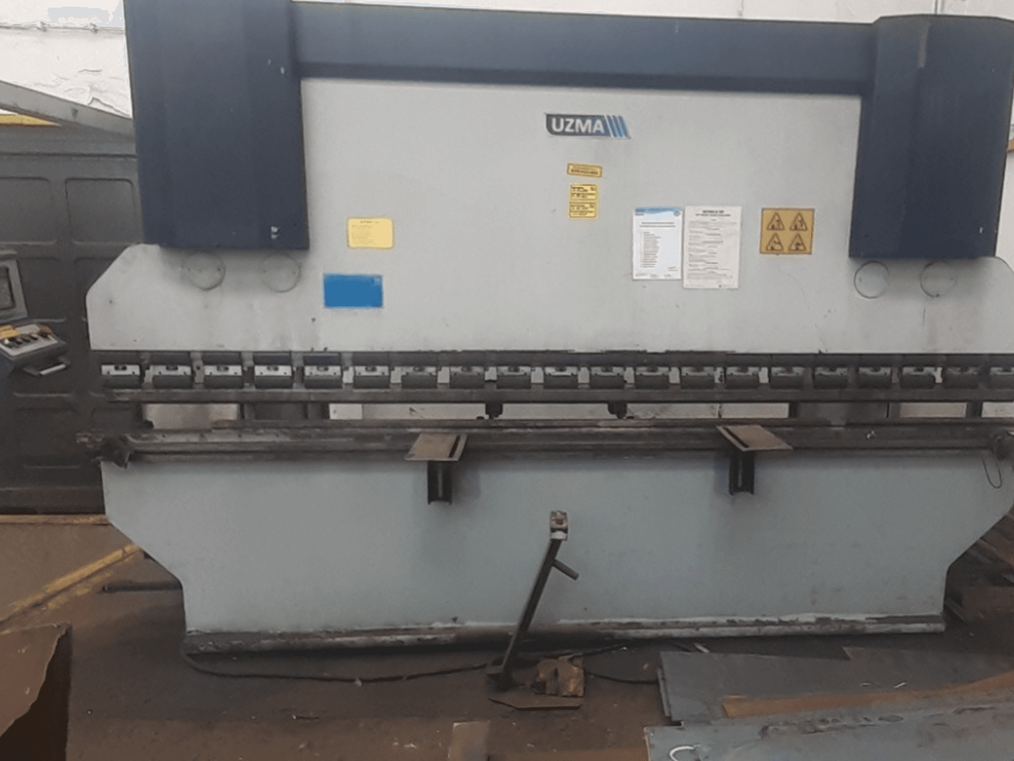 Prasa krawędziowa UZMA HAP 40160 w widoku z przodu, z elementami sterującymi, ostrzeżeniami bezpieczeństwa i narzędziami do gięcia metalu.