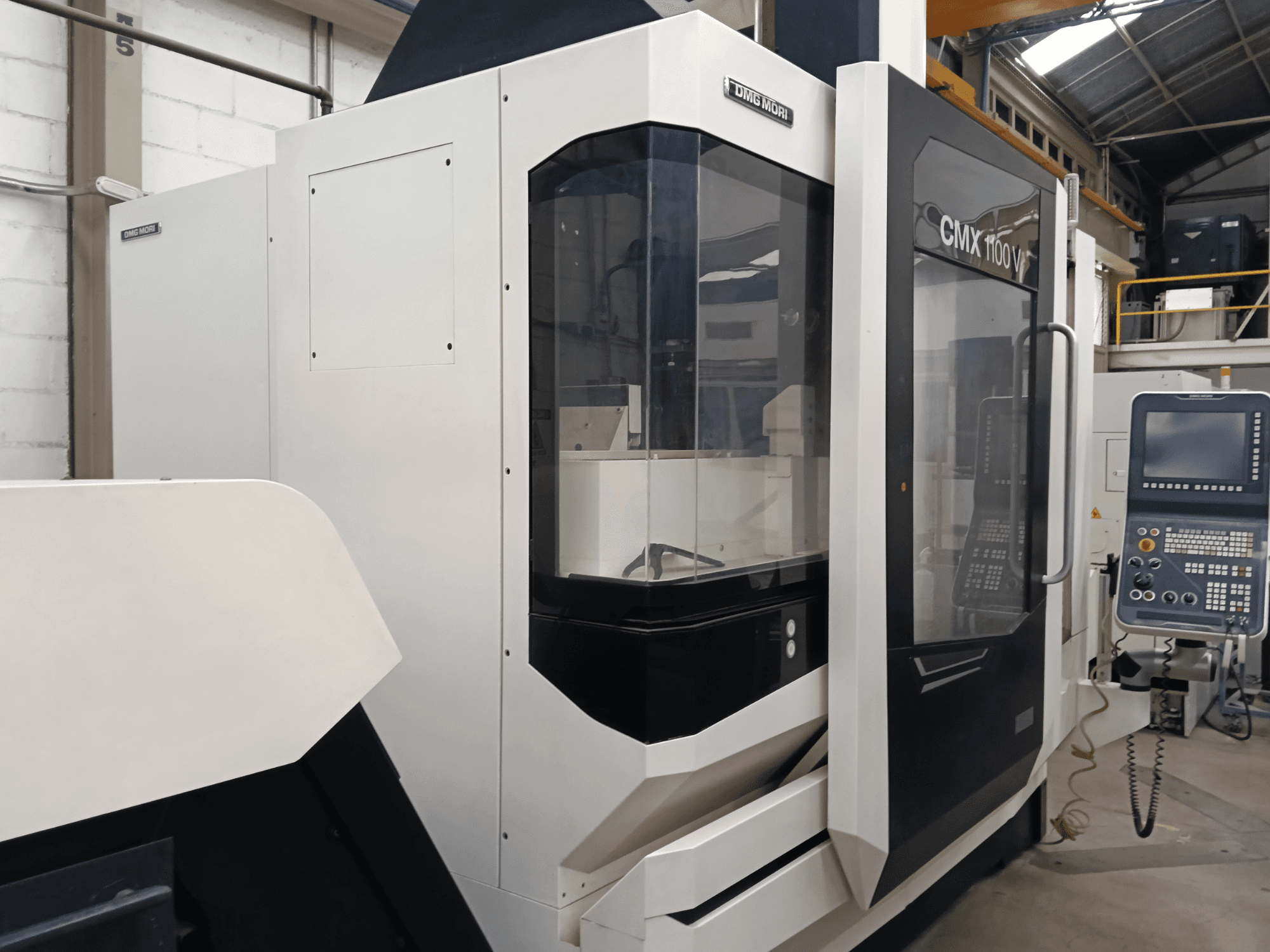 Pionowe centrum obróbcze DMG MORI CMX 1100 V, widok z przodu, przedstawiający panel sterowania i szklaną obudowę.