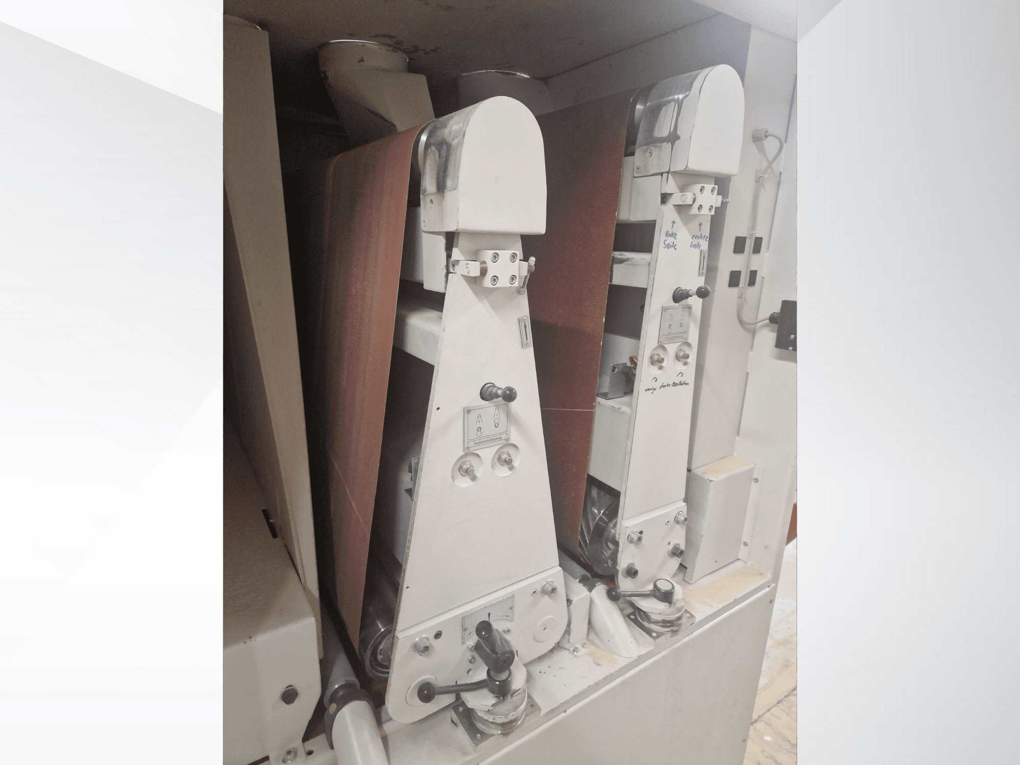 Dwie szlifierki przemysłowe z czerwonymi taśmami szlifierskimi, widok z przodu, z elementami sterującymi i metalowymi.