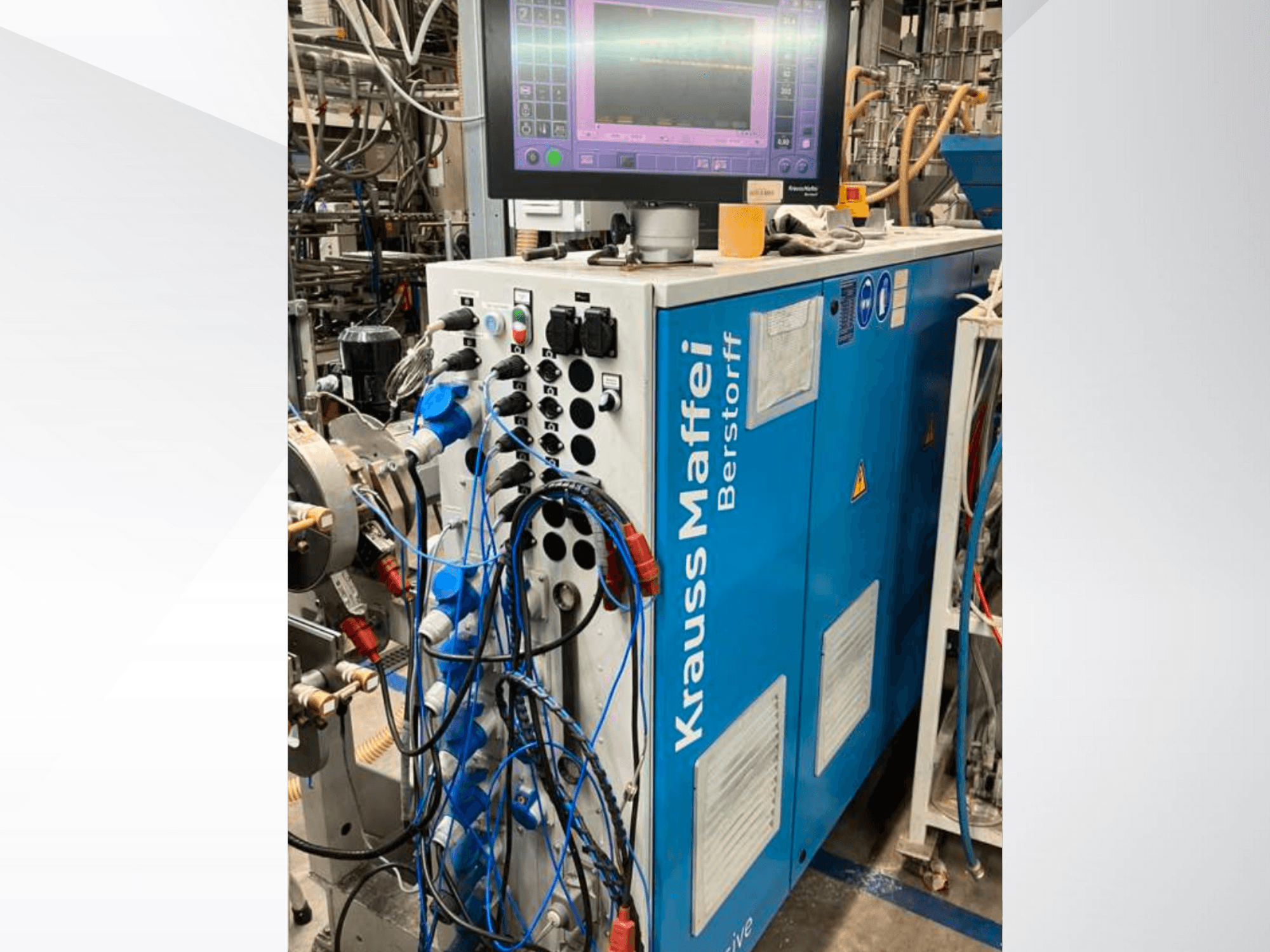 Maszyna przemysłowa Krauss Maffei Berstorff z panelem sterowania i monitorem, z różnymi przyciskami i podłączonymi wężami, widok z boku.