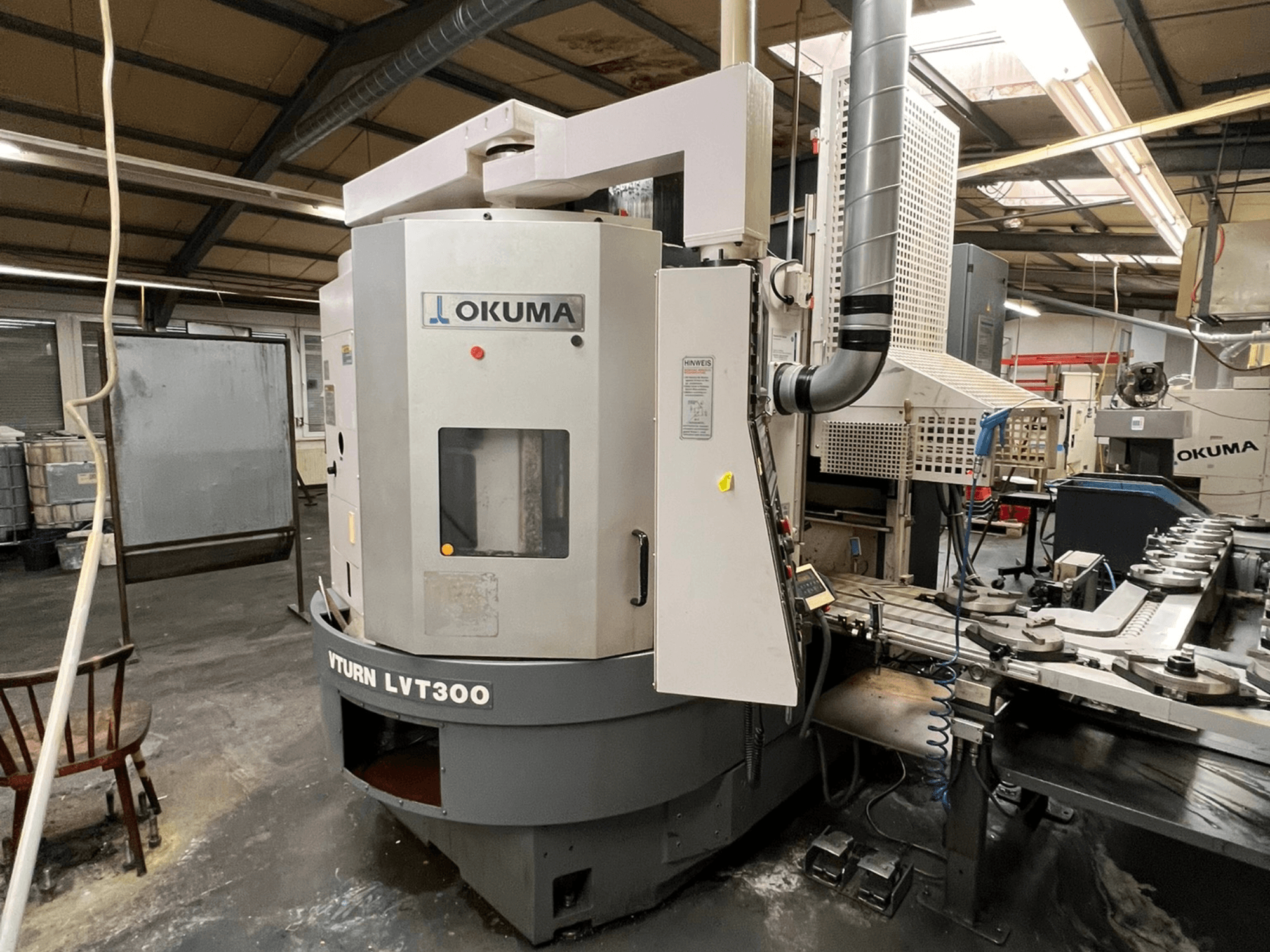 Tokarka CNC Okuma Vturn LVT300, widok z boku w otoczeniu przemysłowym, z panelem sterowania i układem chłodzenia.