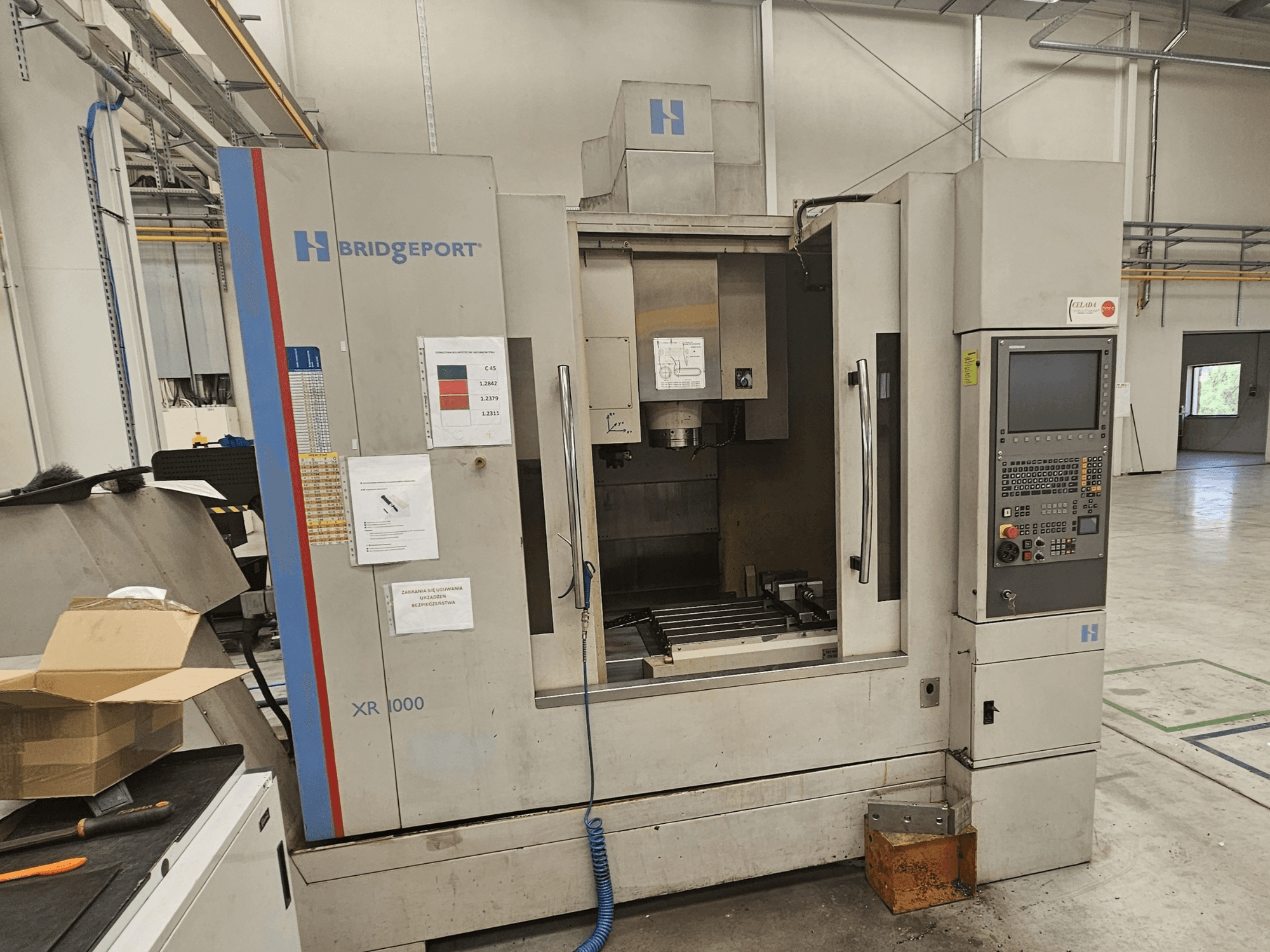 Pionowe centrum obróbcze Bridgeport XR 1000, widok z przodu, z panelem sterowania i widocznym obszarem roboczym ze stołem do cięcia.